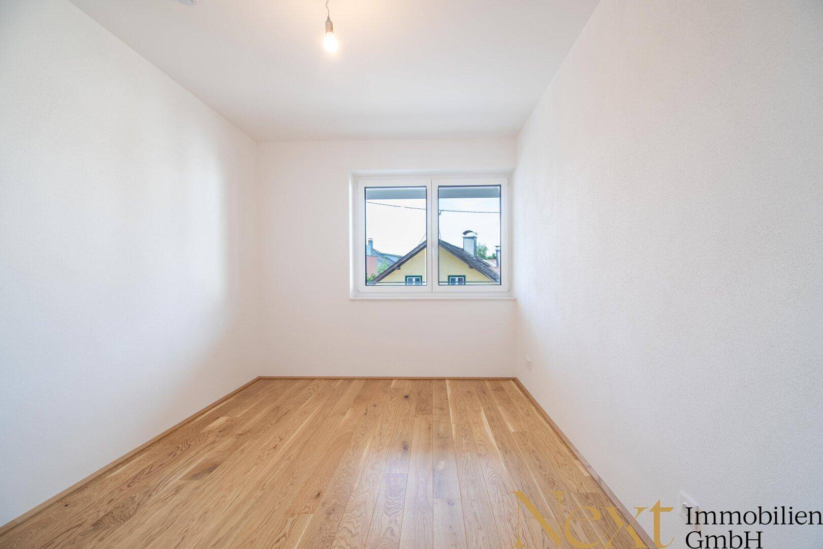 Gemütliches Zimmer mit Parkettboden und einem Fenster, das einen Blick ins Grüne bietet.