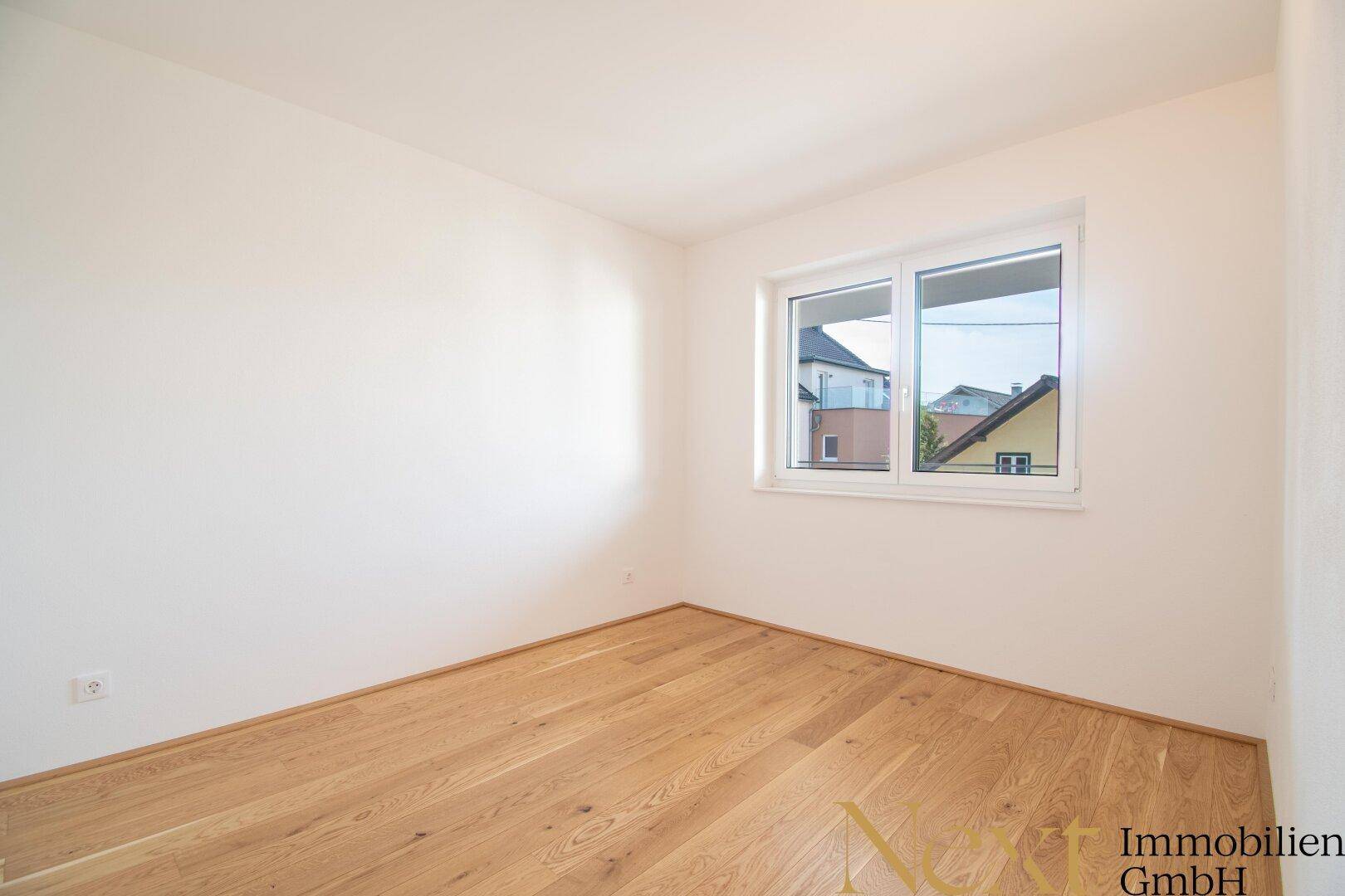 Helles Schlafzimmer mit Eichenparkett und einem Fenster, das für eine angenehme Atmosphäre sorgt.
