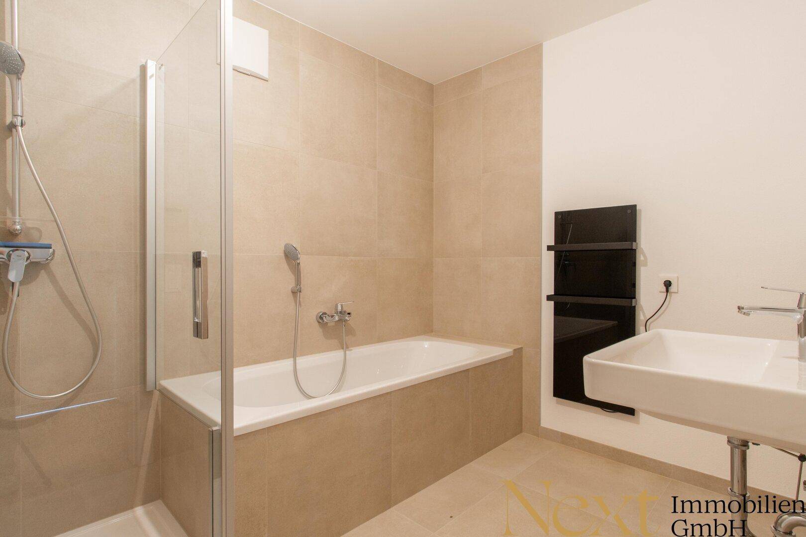 Modernes Badezimmer mit Badewanne, Duschkabine und Waschbecken, in hellen Beigetönen gefliest.