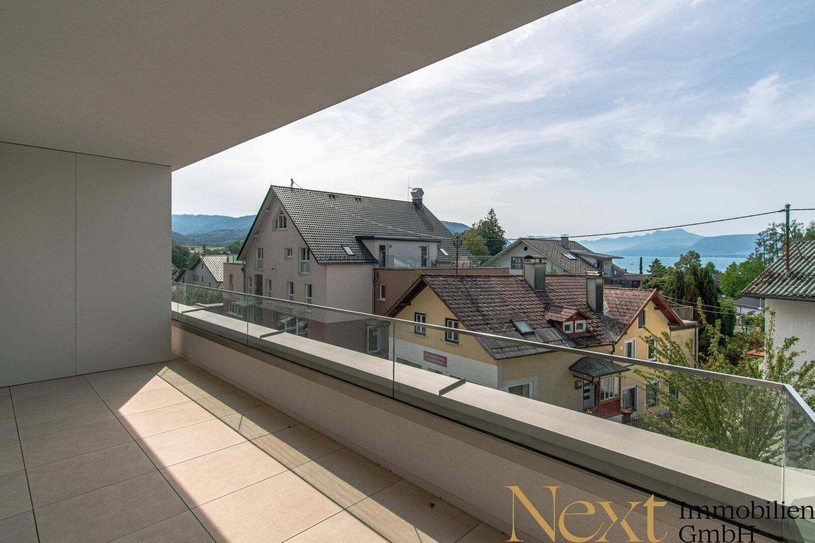 Geräumiger Balkon mit Glasbrüstung und weitem Blick über die Dächer zum See.