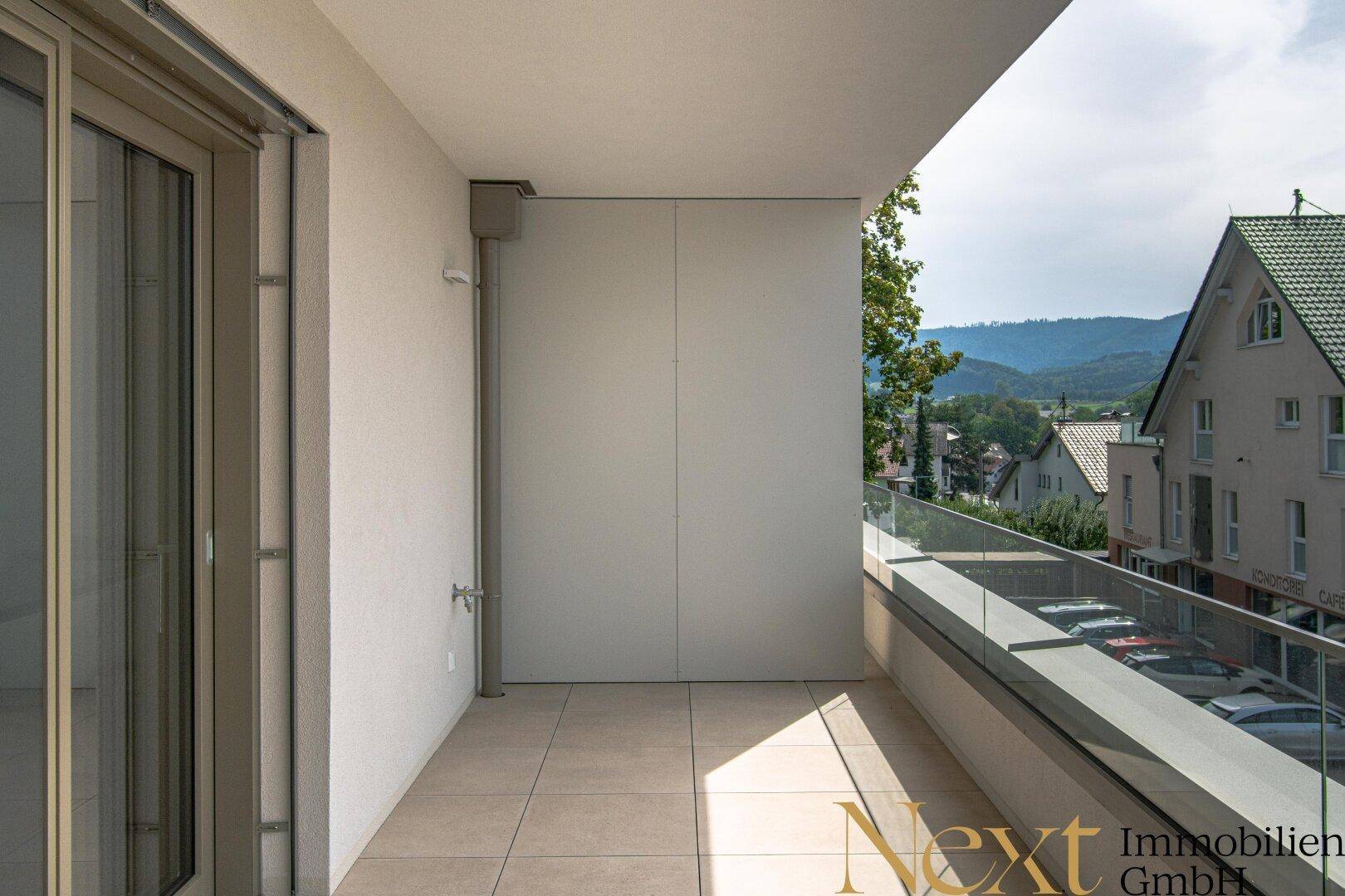 Heller, gefliester Balkon mit moderner Glasbrüstung und seitlichem Bergblick.