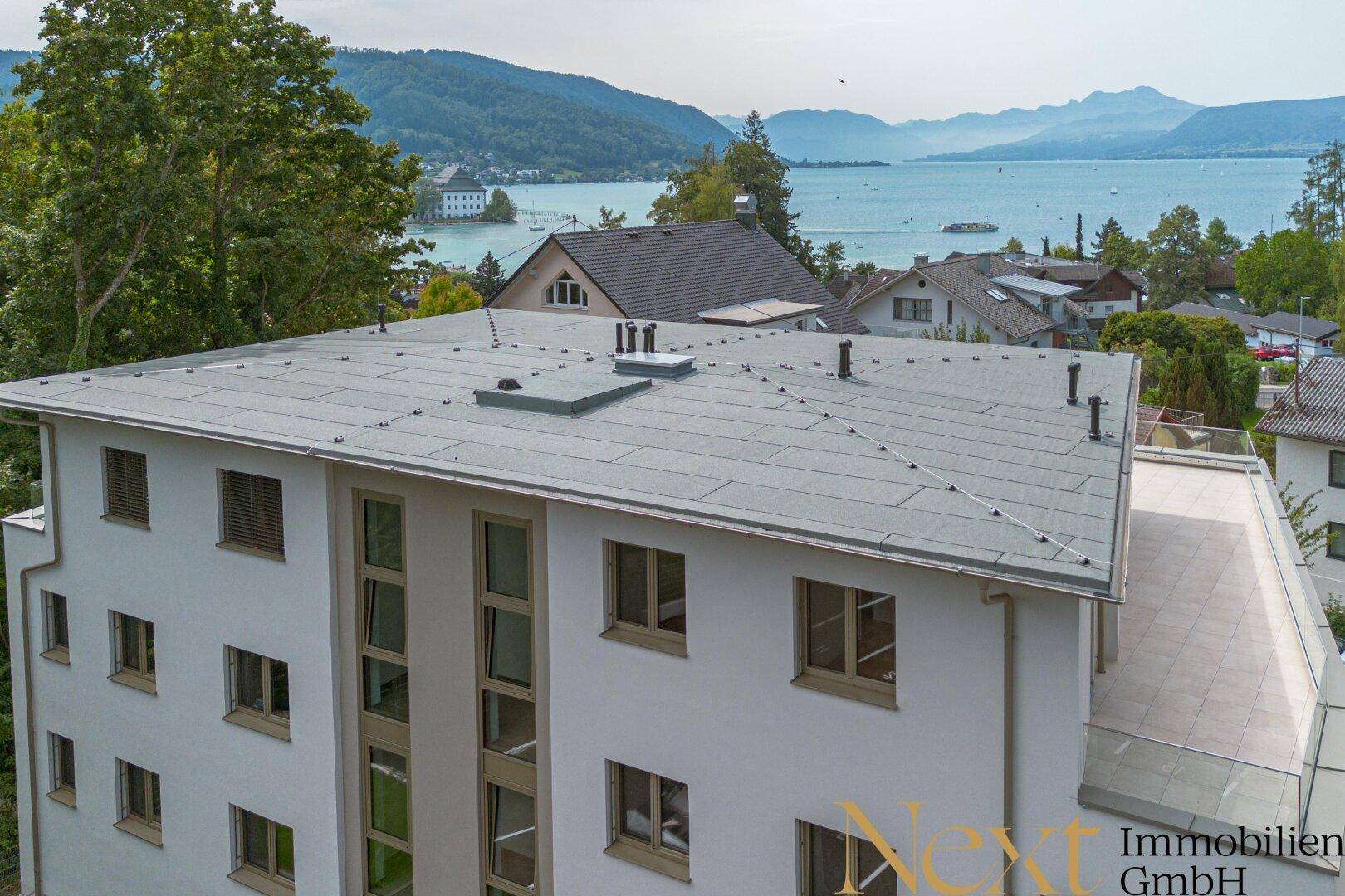 Dachansicht eines modernen Gebäudes mit Flachdach und Seeblick im Hintergrund.
