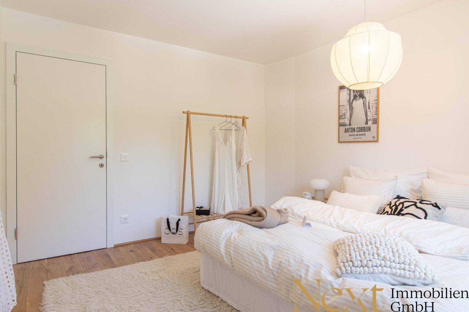 Gemütliches Schlafzimmer mit Holzboden, weißem Bett und minimalistischer Kleiderstange.