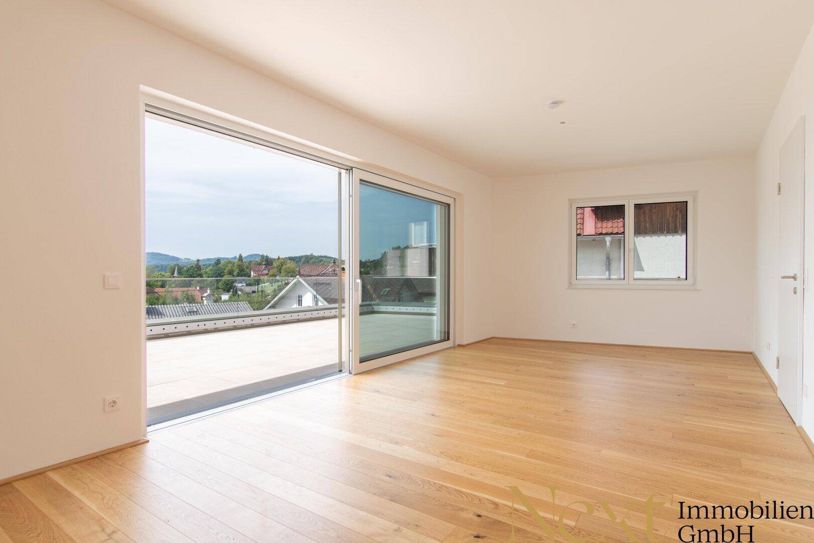 Heller, leerer Wohnbereich mit großen Schiebetüren zur Terrasse und schönem Holzboden.