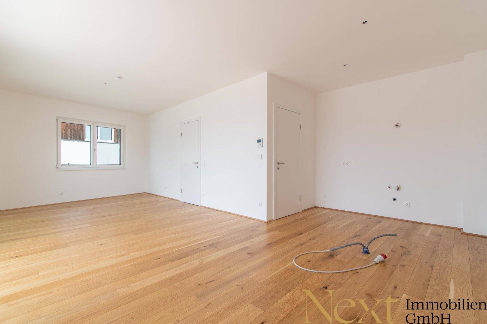 Leerer Küchenbereich mit vorbereiteten Anschlüssen für eine moderne Einbauküche und Holzboden.