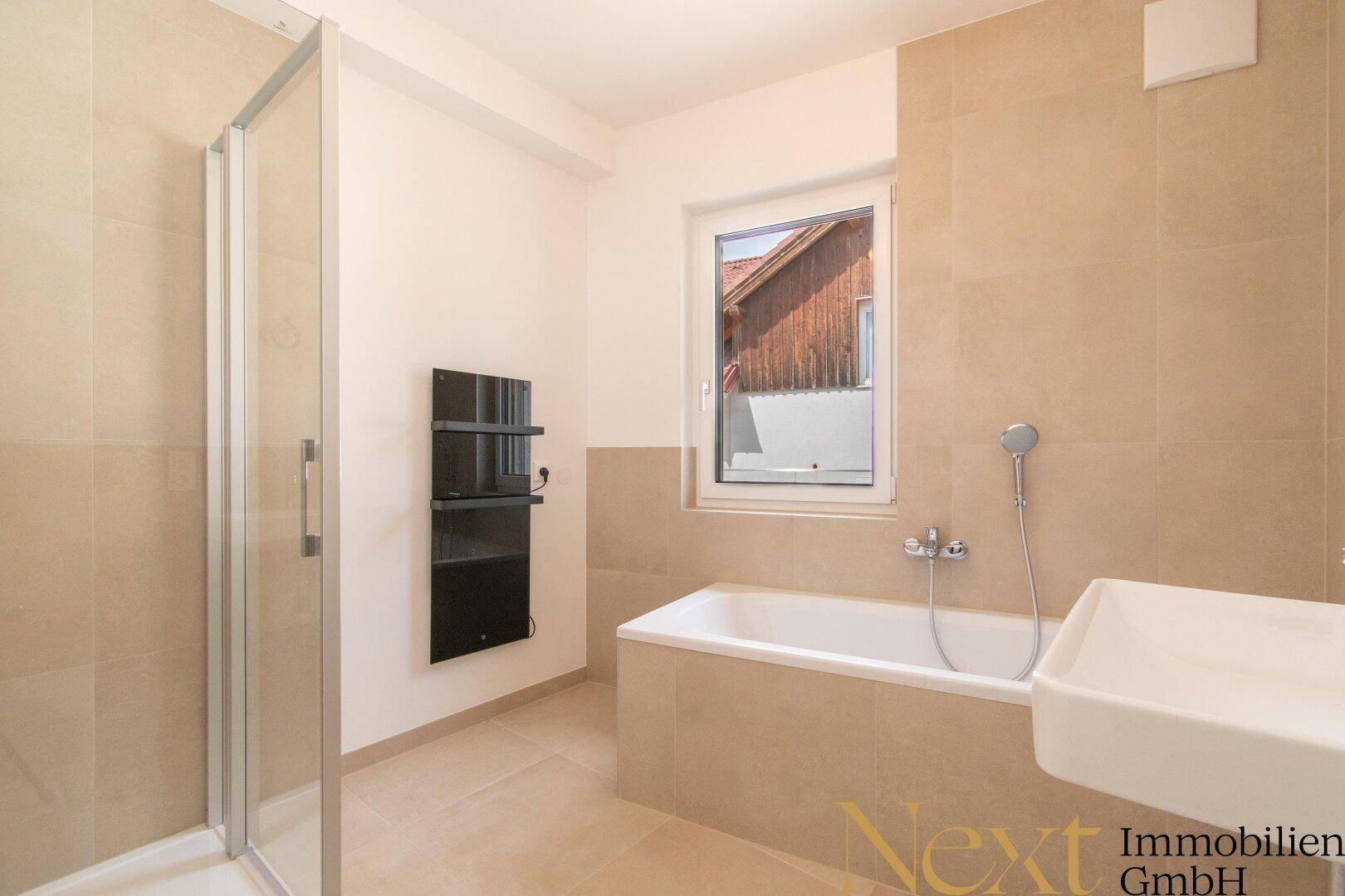 Modernes Badezimmer mit Badewanne, Dusche, Fenster und beheiztem Handtuchhalter.