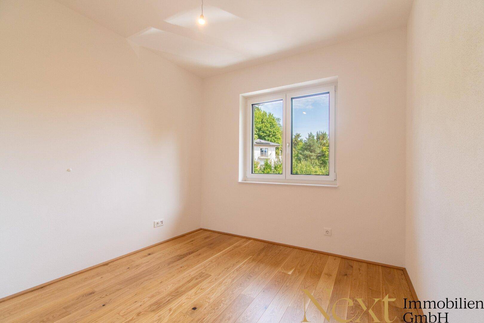 Ruhiges Schlafzimmer mit Holzboden und einem Fenster mit Blick ins Grüne.