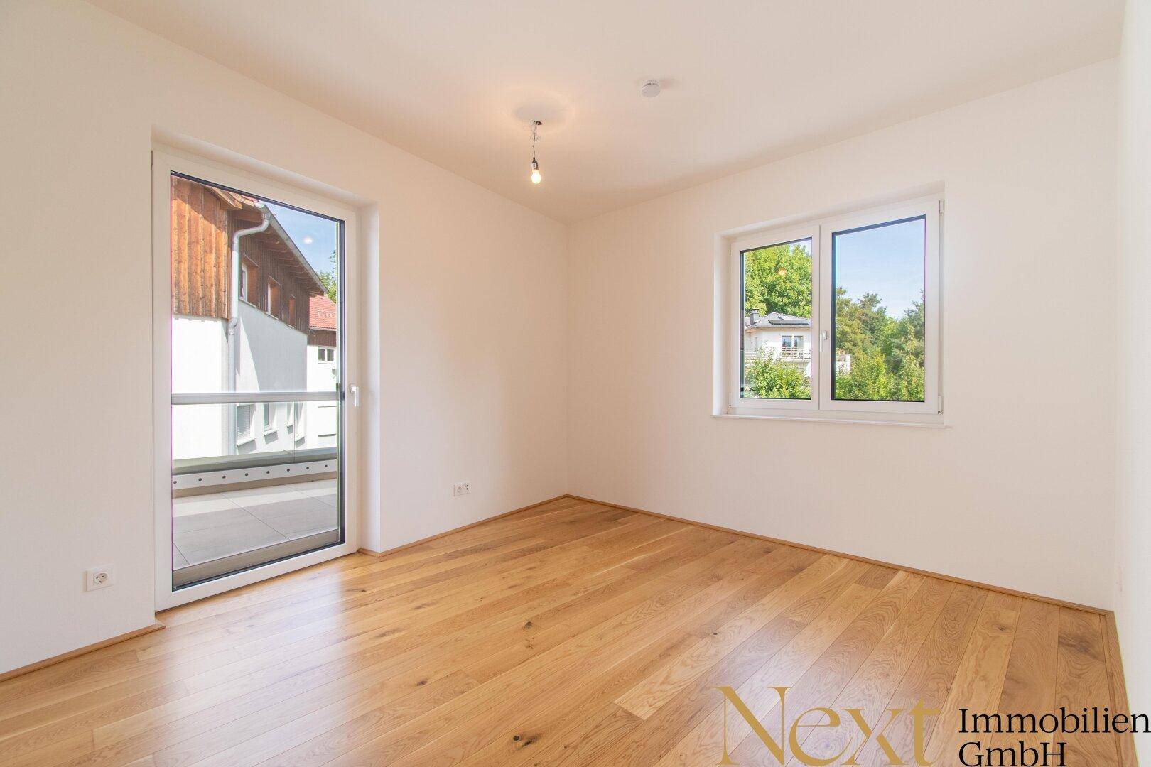 Helles Schlafzimmer mit Holzboden und Zugang zu einem kleinen Balkon oder einer Terrasse.
