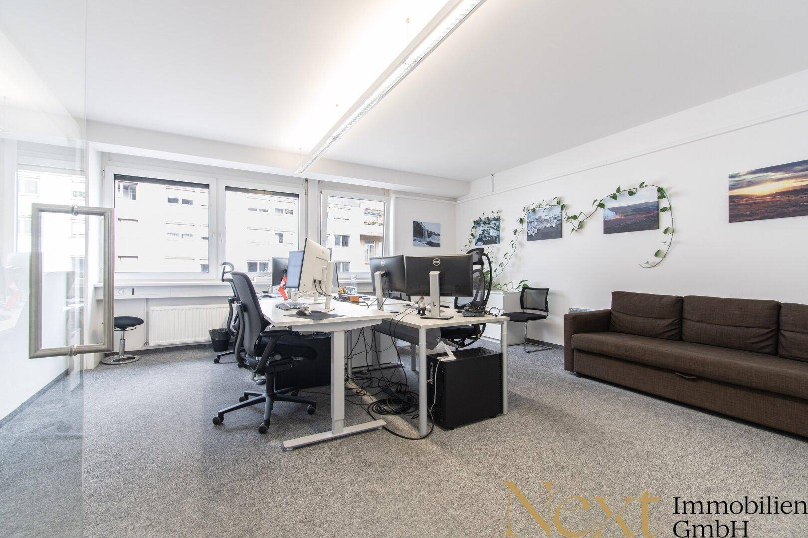 Geräumiges Büro mit mehreren Schreibtischen, Computern und einem Sofa, ideal für Teamarbeit.