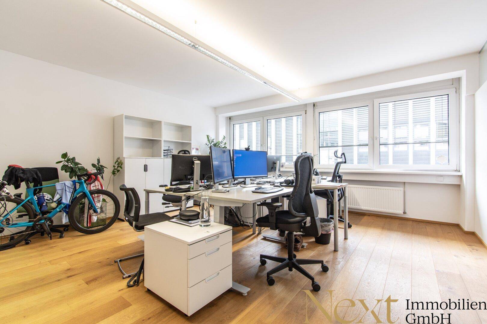Modernes Büro mit Holzboden, mehreren Arbeitsplätzen und einem Fahrrad, das eine dynamische Atmosphäre schafft.