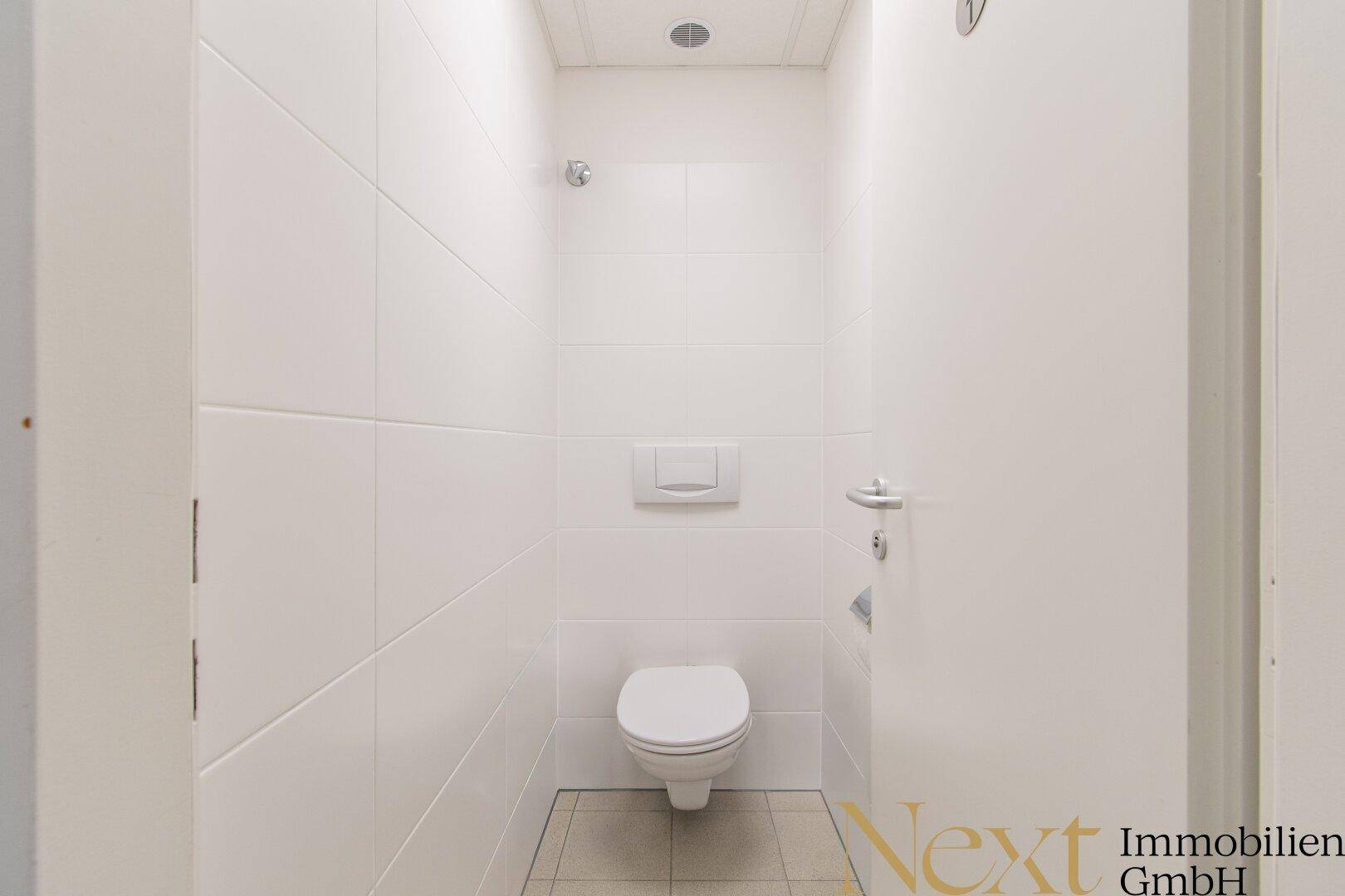 Saubere und helle Toilette mit Wand-WC und weißen Fliesen, minimalistisch gestaltet.