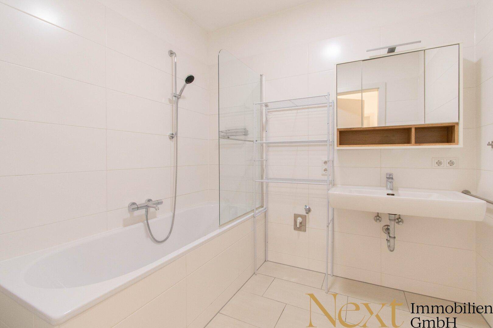 Modernes Badezimmer mit Badewanne, Dusche und Spiegelschrank in hellen Fliesen.