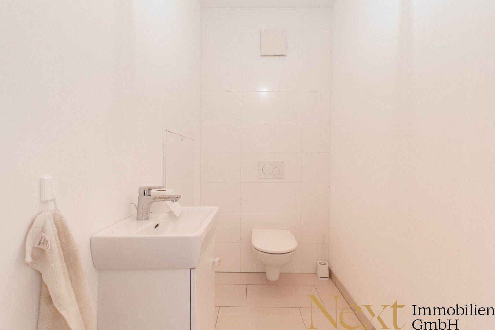Separates Gäste-WC mit wandhängender Toilette und kleinem Waschbecken in minimalistischem Design.