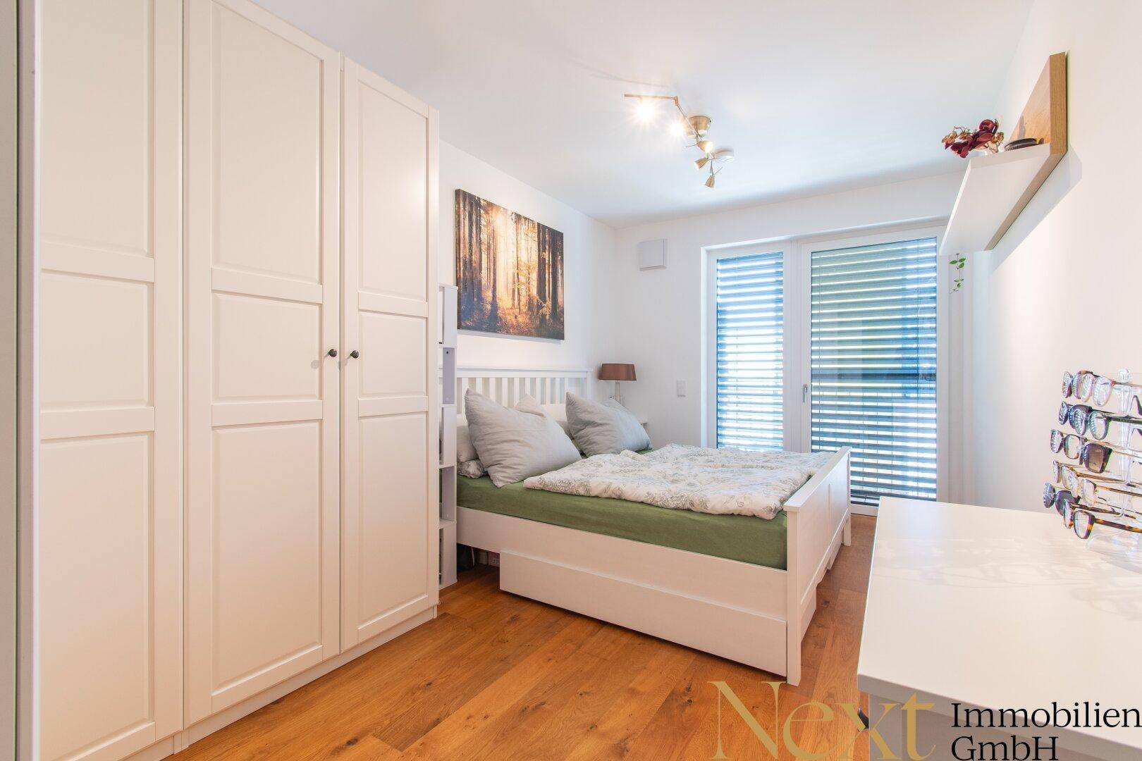 Gemütliches Schlafzimmer mit Holzboden, weißem Kleiderschrank und Balkonzugang.