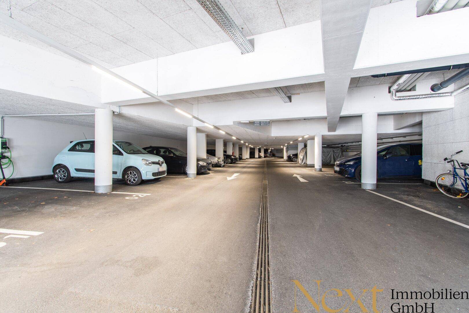 Helle Tiefgarage mit markierten Stellplätzen und Ladestation für Elektrofahrzeuge.