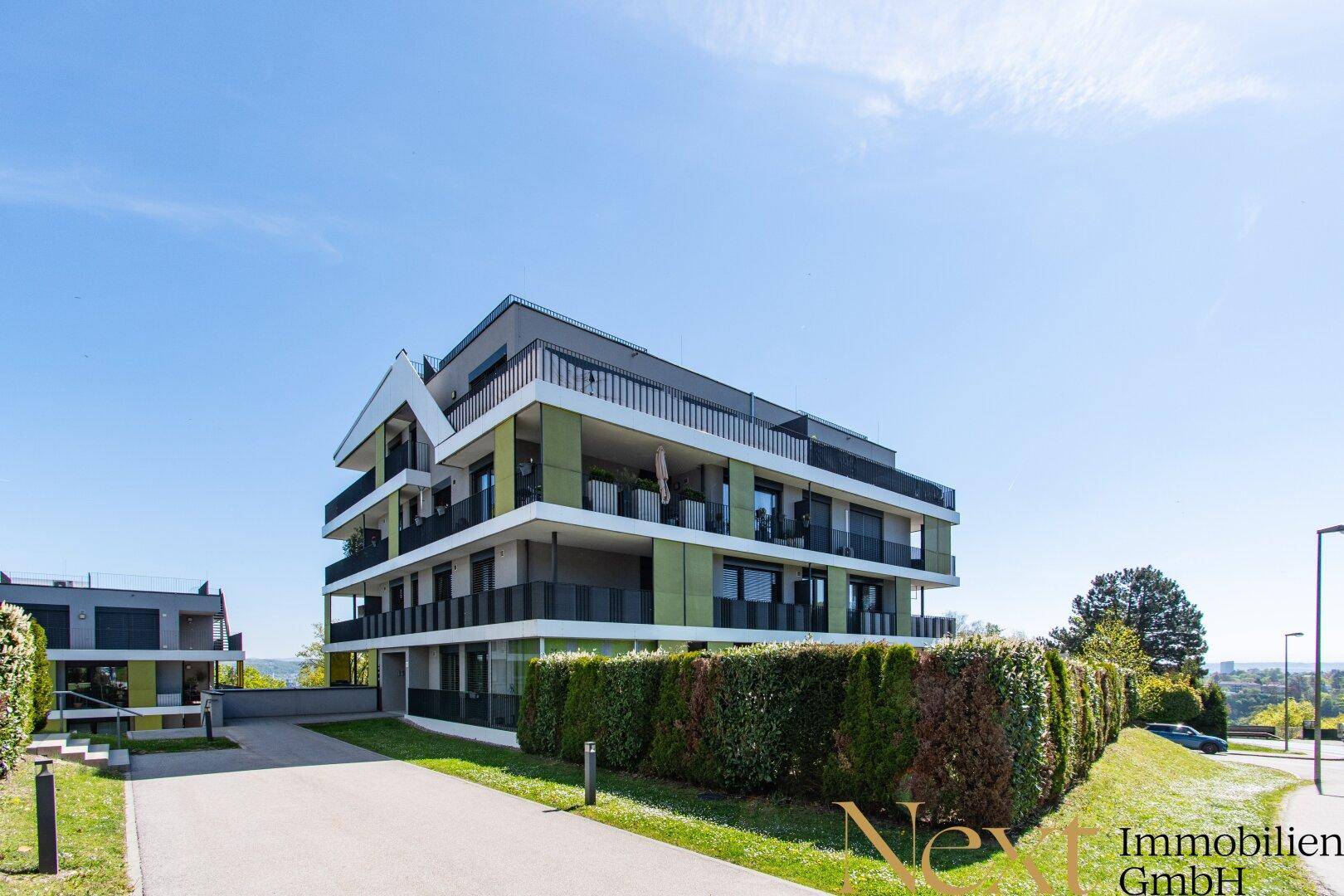 Modernes Mehrfamilienhaus mit grünen Akzenten und gepflegter Außenanlage unter blauem Himmel.