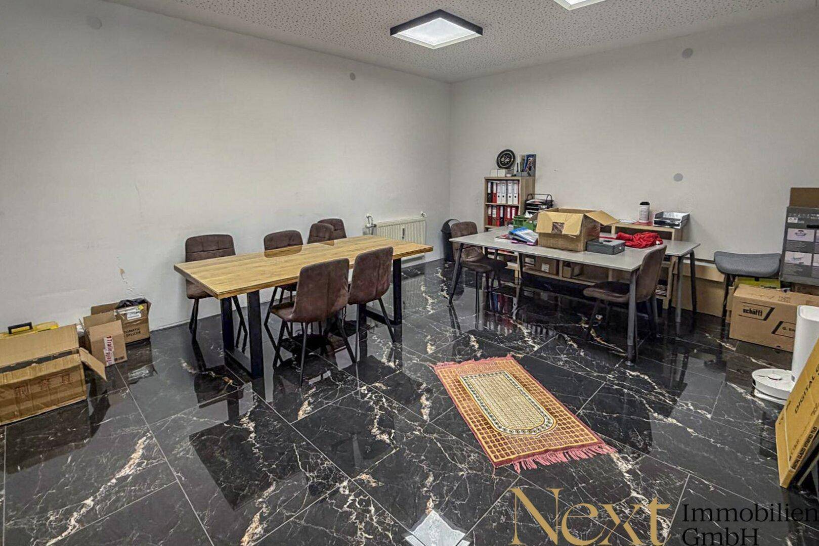 Besprechungsraum mit dunklem Marmorboden, großem Holztisch und Büromöbeln, gut beleuchtet.