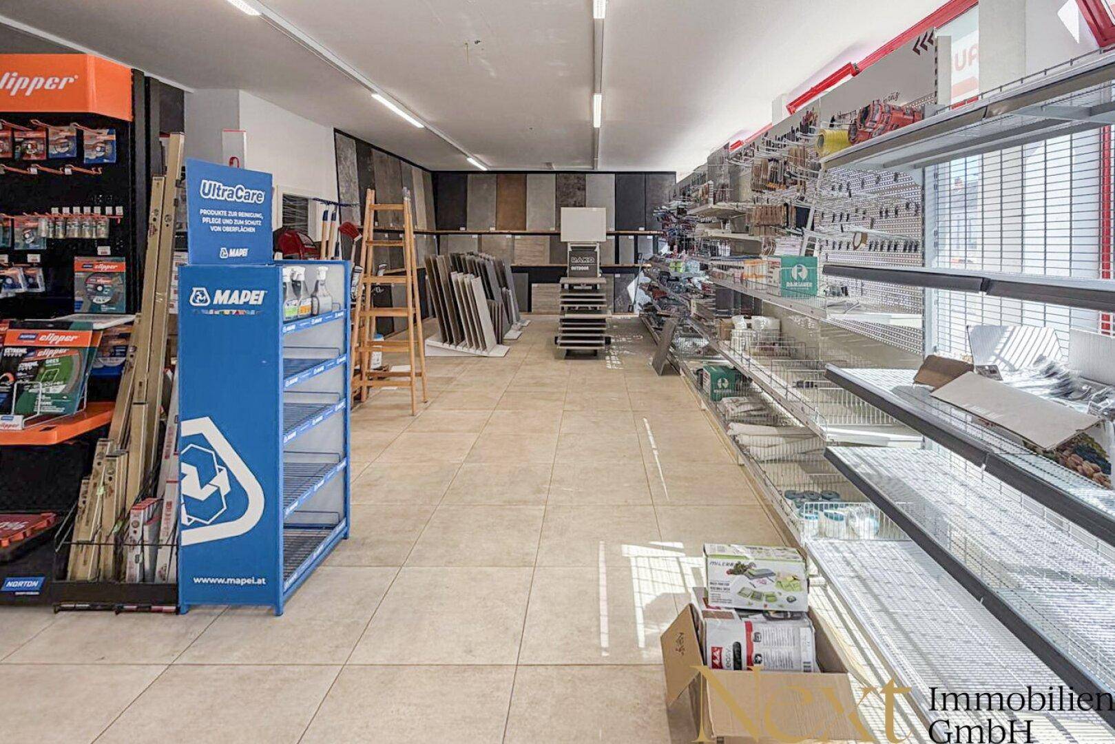 Langer Verkaufsraum mit Fliesenboden, Regalen und Produktpräsentationen, gut beleuchtet.