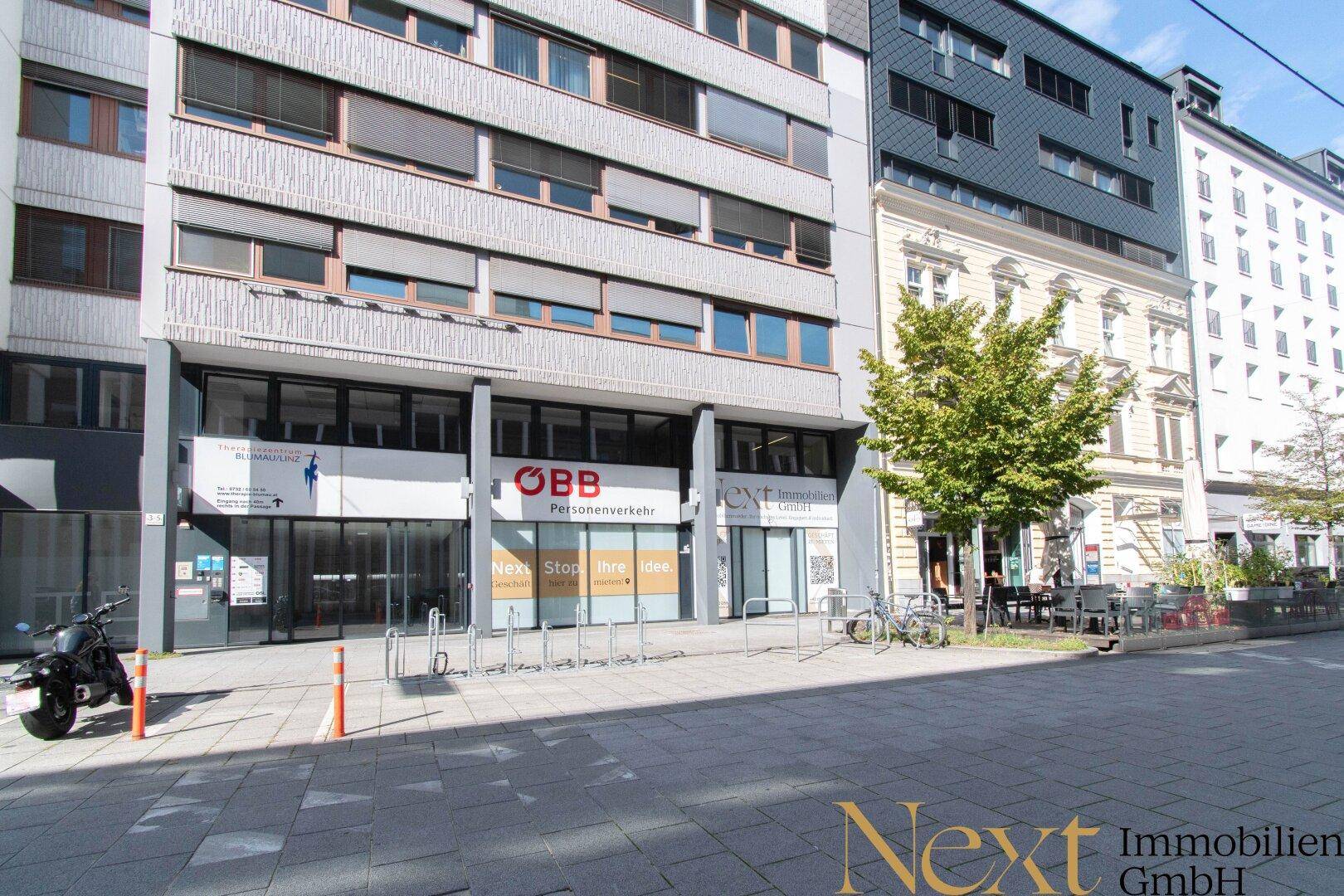 Breitere Ansicht der Geschäftsgebäude an einer belebten Straße mit Cafés und Fahrradständern.