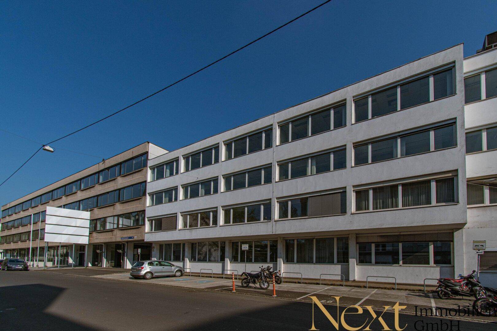 Modernes Bürogebäude mit mehreren Etagen und großen Fensterfronten an einer städtischen Straße.