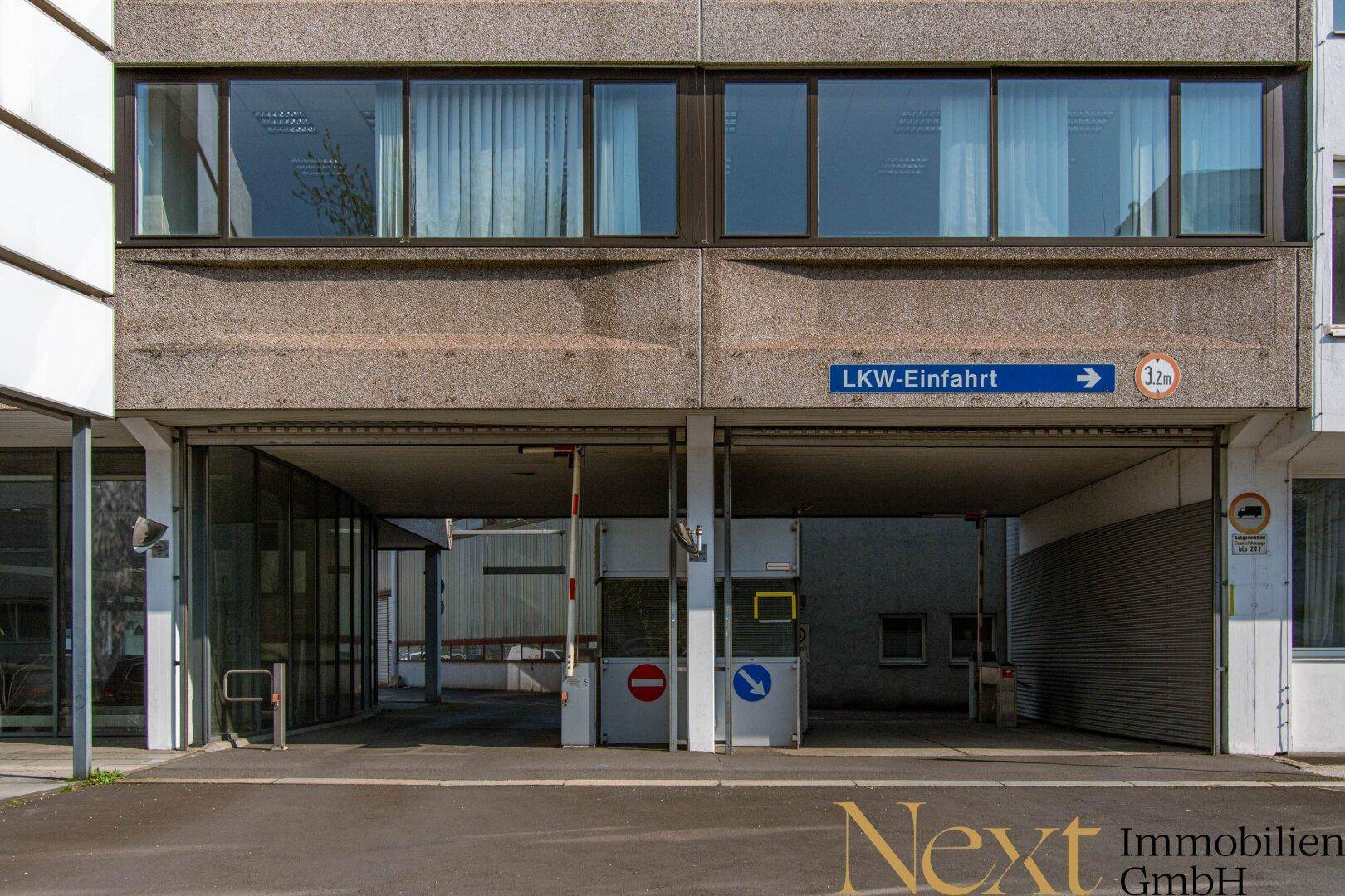 Einfahrt für Lastkraftwagen zu einem Gewerbegebäude mit Betonfassade und Hinweisschildern.