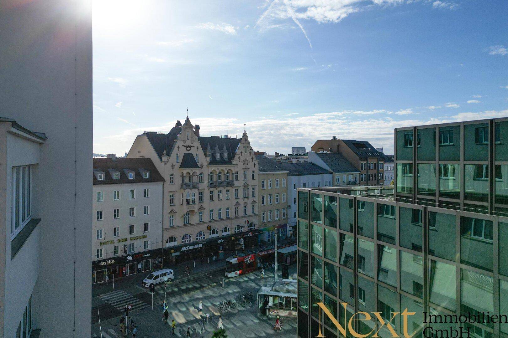 Weitläufiger Stadtblick über belebte Straßen und historische Gebäude bei Sonnenschein.