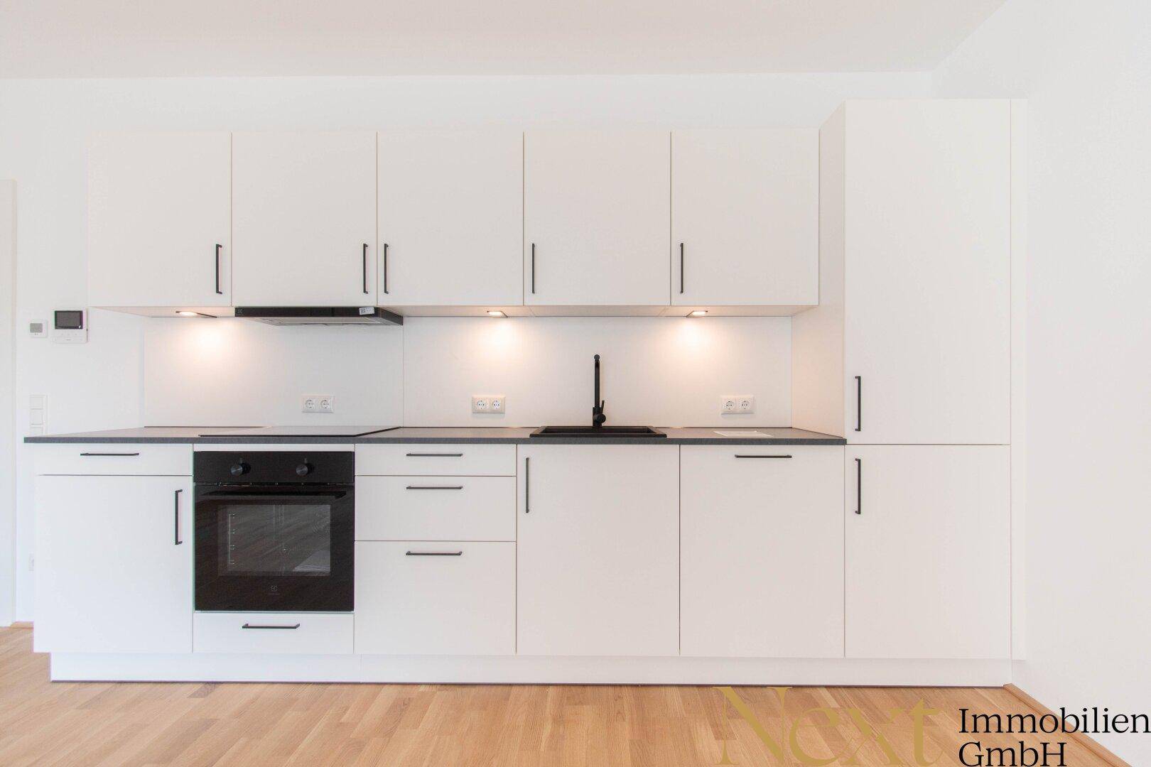 Moderne Einbauküche in Weiß mit dunkler Arbeitsplatte und integriertem Backofen.