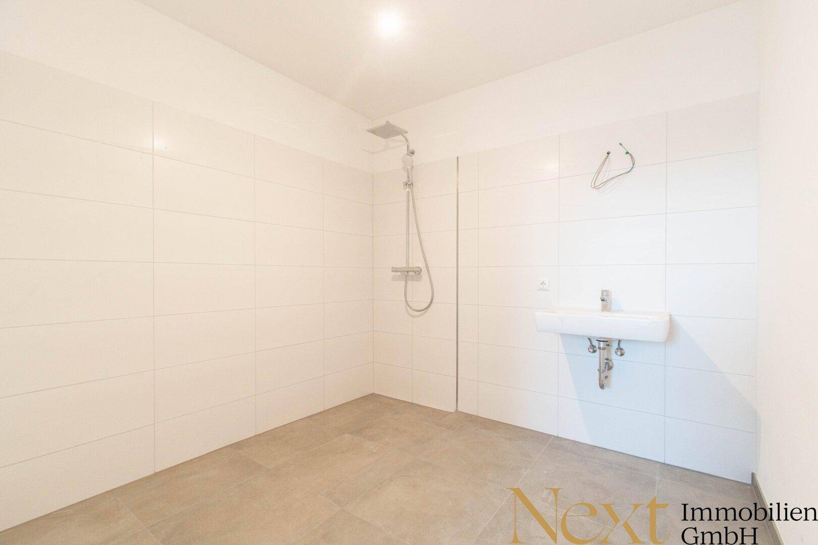Helles Badezimmer mit moderner Dusche, weiß gefliesten Wänden und einem Waschbecken.