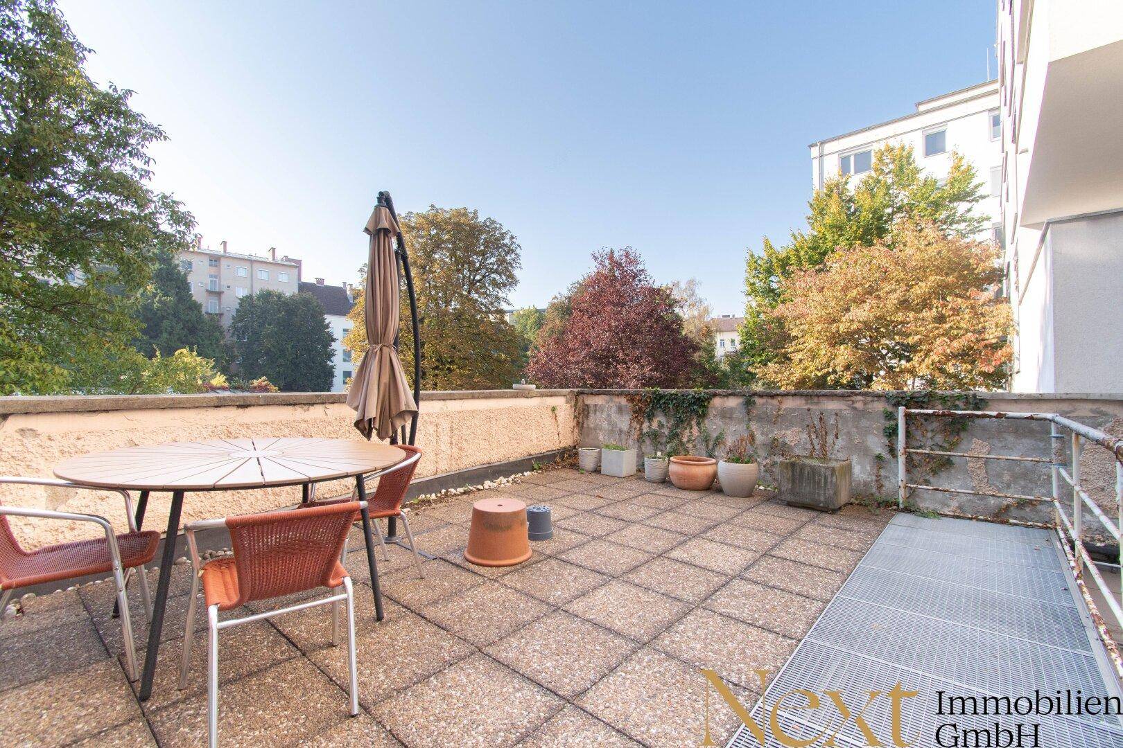Sonniger Terrassenbereich mit Sitzgelegenheiten, Sonnenschirm und weitem Blick ins Grüne.