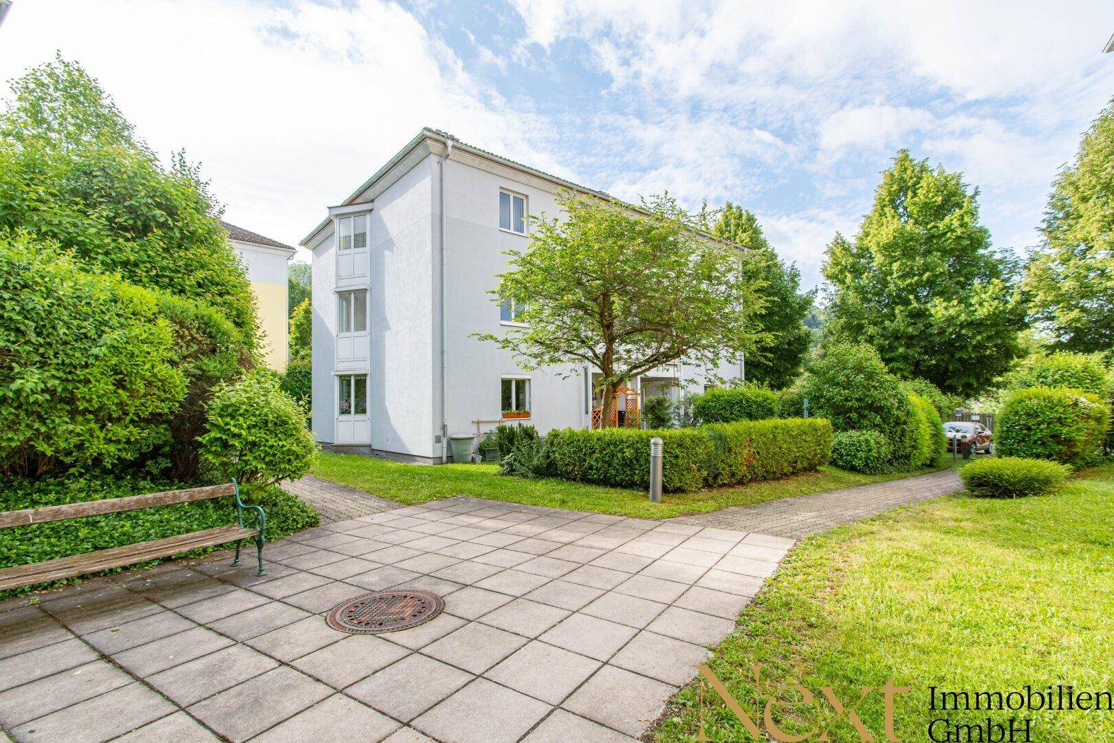 Ruhige Wohnanlage mit viel Grün, gepflegten Rasenflächen und einem Mehrfamilienhaus.