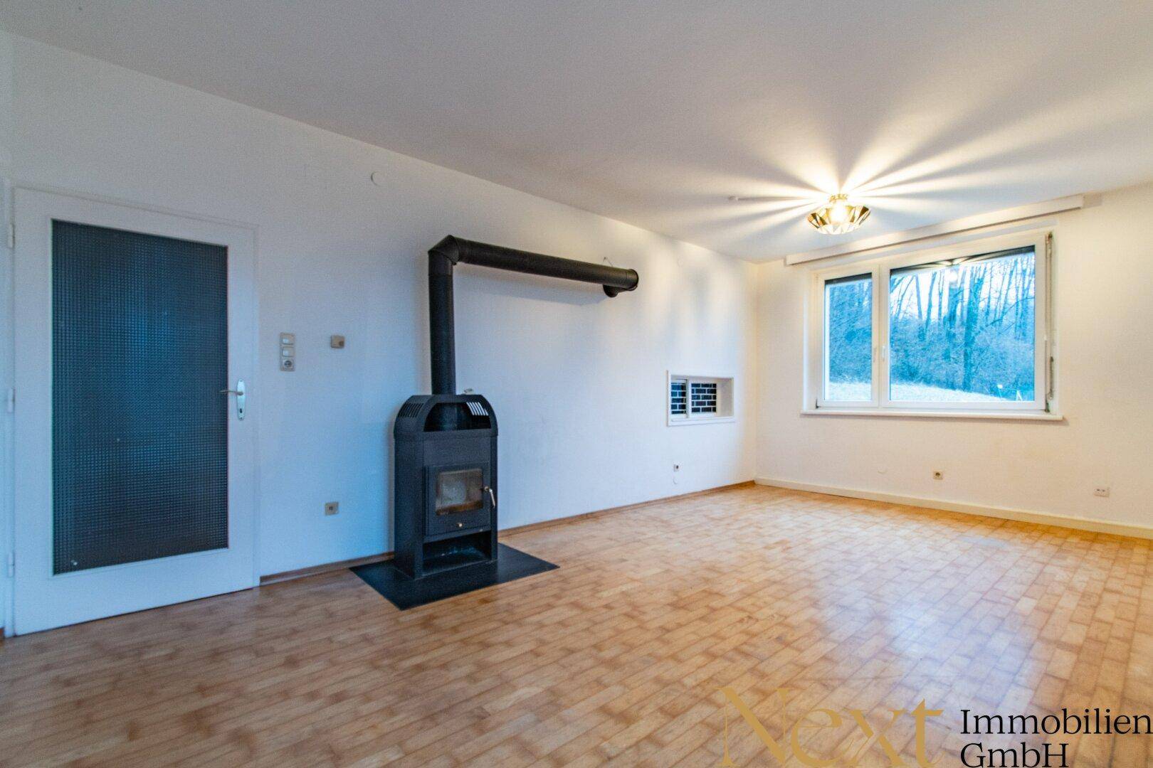 Leeres Wohnzimmer mit Holzofen, hellen Wänden und Parkettboden.