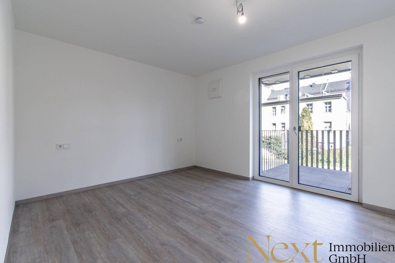 Heller Raum mit Zugang zu einem Balkon und modernem Laminatboden.