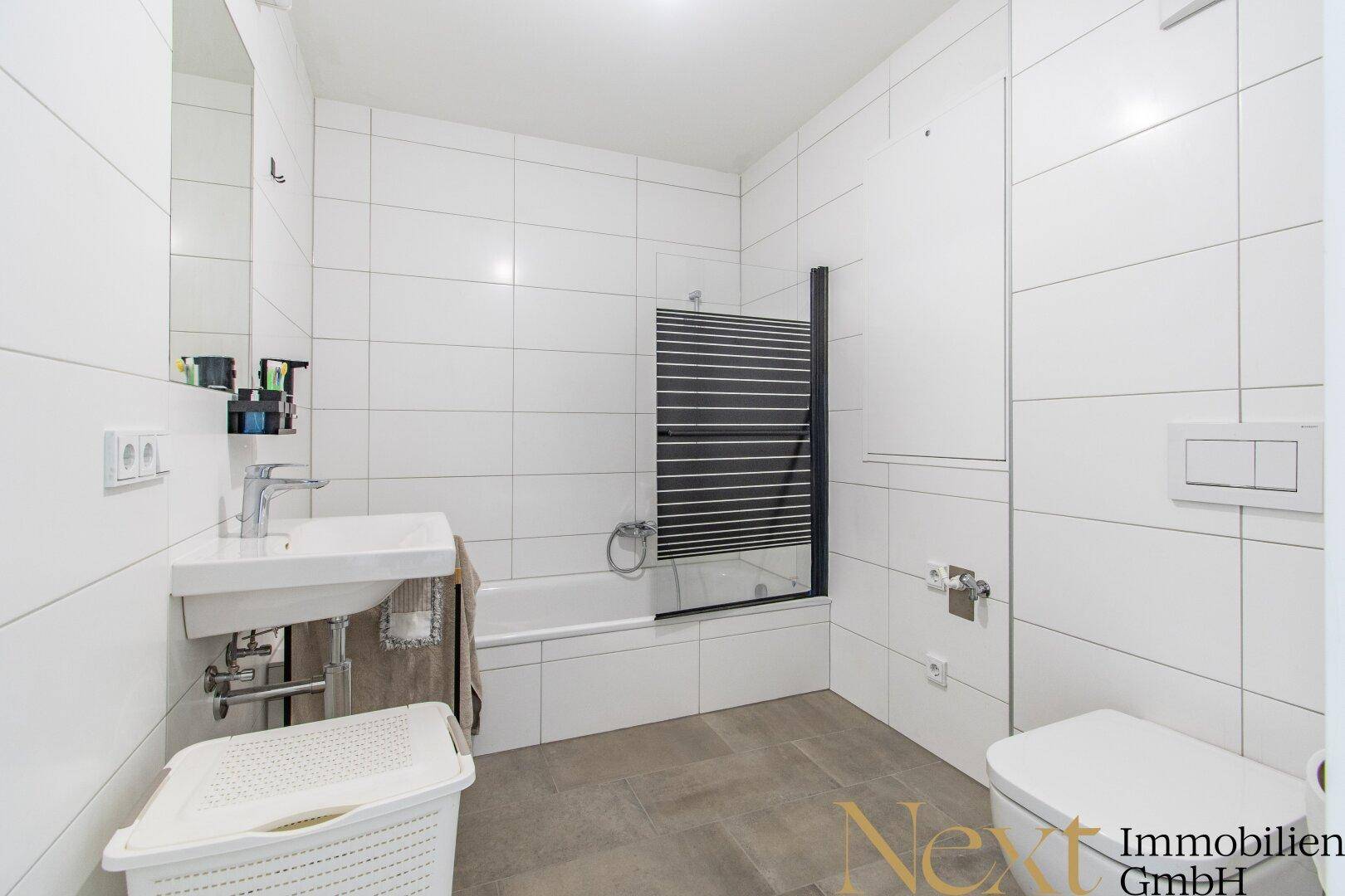 Modernes Badezimmer mit weißen Fliesen, Badewanne und integrierter Dusche.