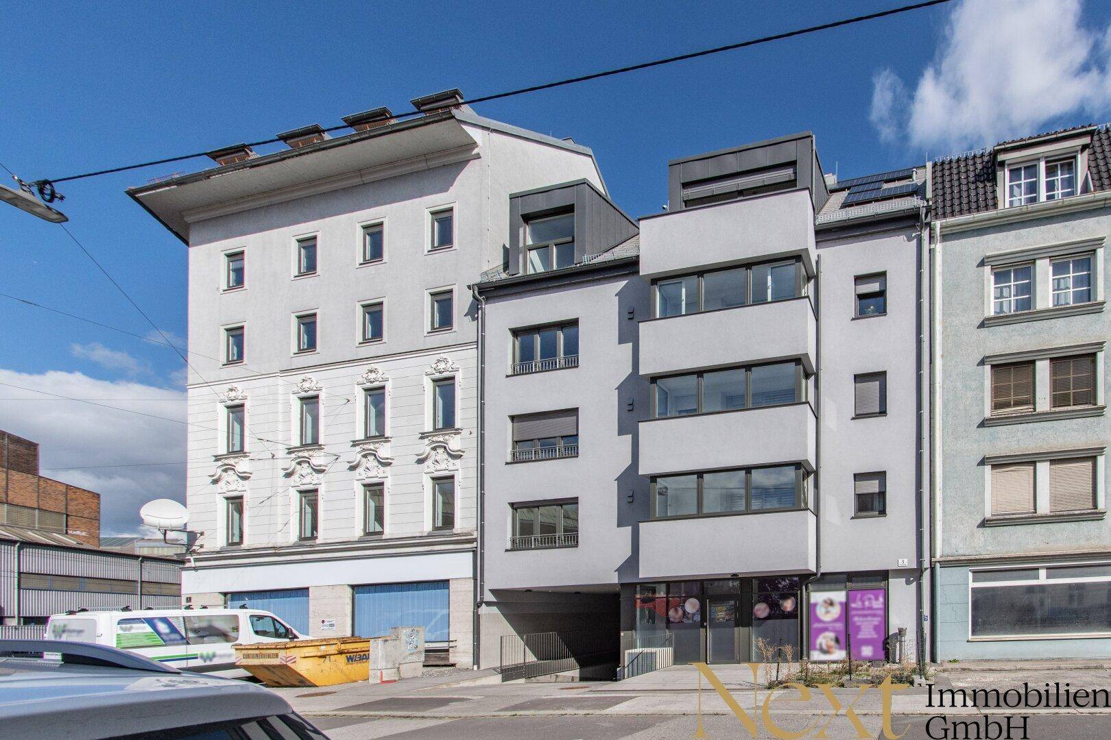 Moderne Gebäudefassade mit großen Fenstern und angrenzenden Altbauten.