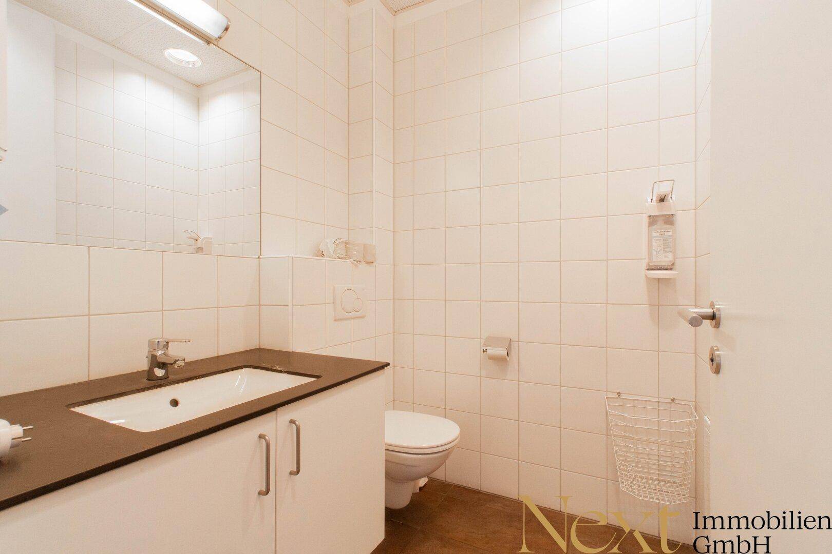 Modernes Badezimmer mit Waschtisch, Spiegel, Toilette und weißen Wandfliesen, sauber und gepflegt.