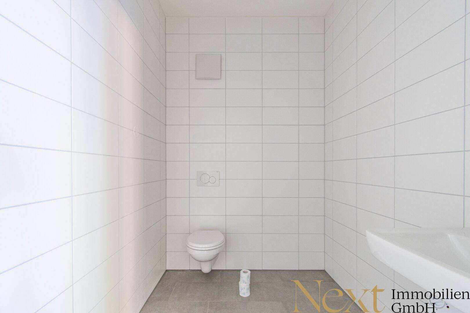 Modern gefliestes Gäste-WC mit wandhängender Toilette und Lüftungsgitter, in sauberem und neuwertigem Zustand.