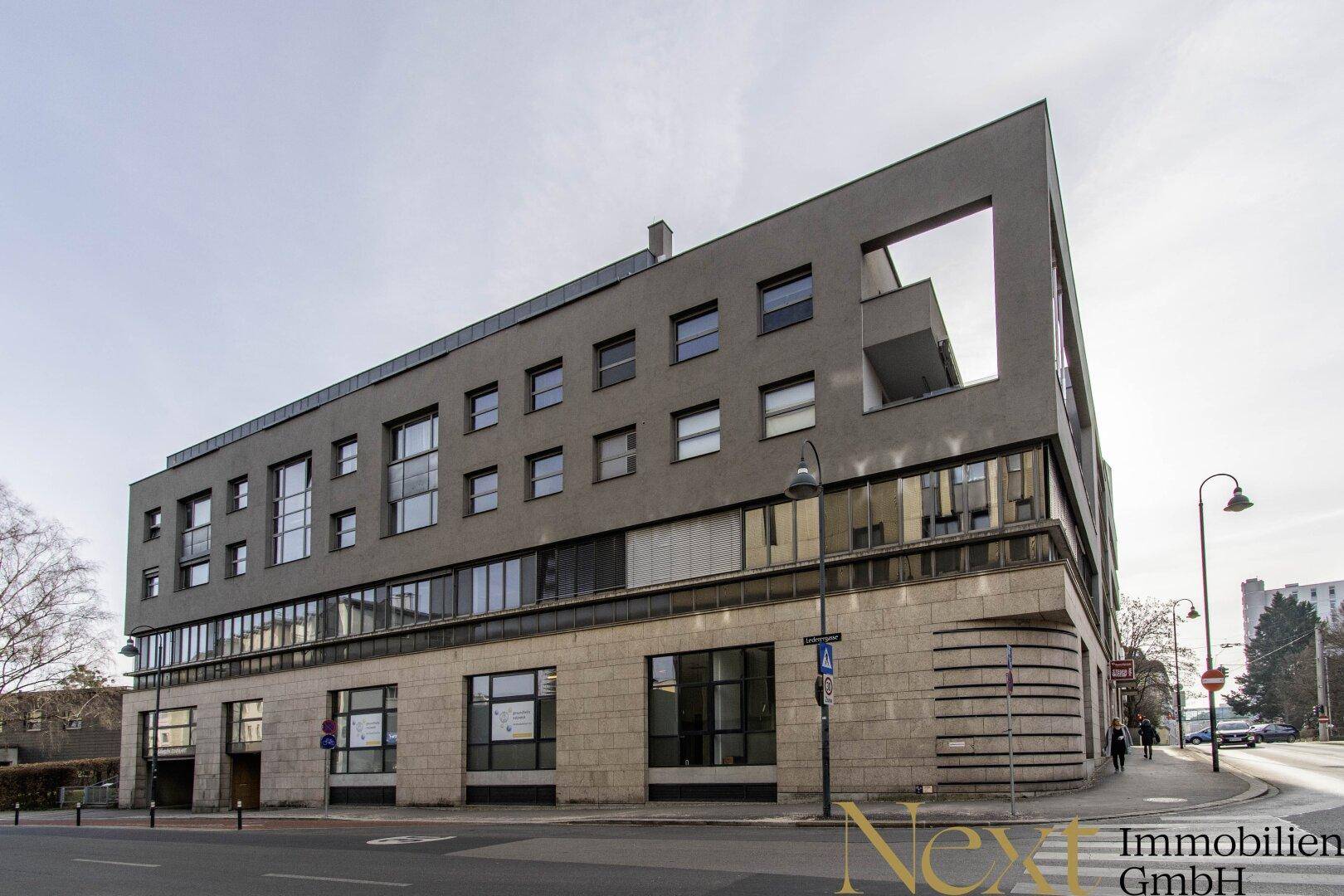 Modernes Geschäftsgebäude mit markanter Architektur, großen Fenstern und Steinfassade im Erdgeschoss.