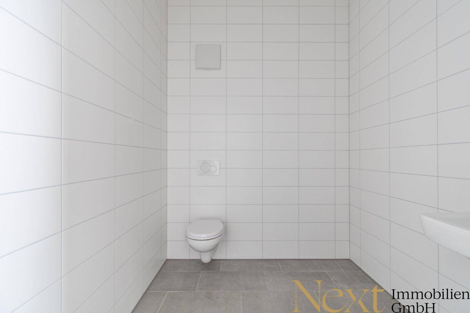 Sauberes Gäste-WC mit weißen Fliesen an den Wänden und grauem Boden, minimalistisch und funktional.