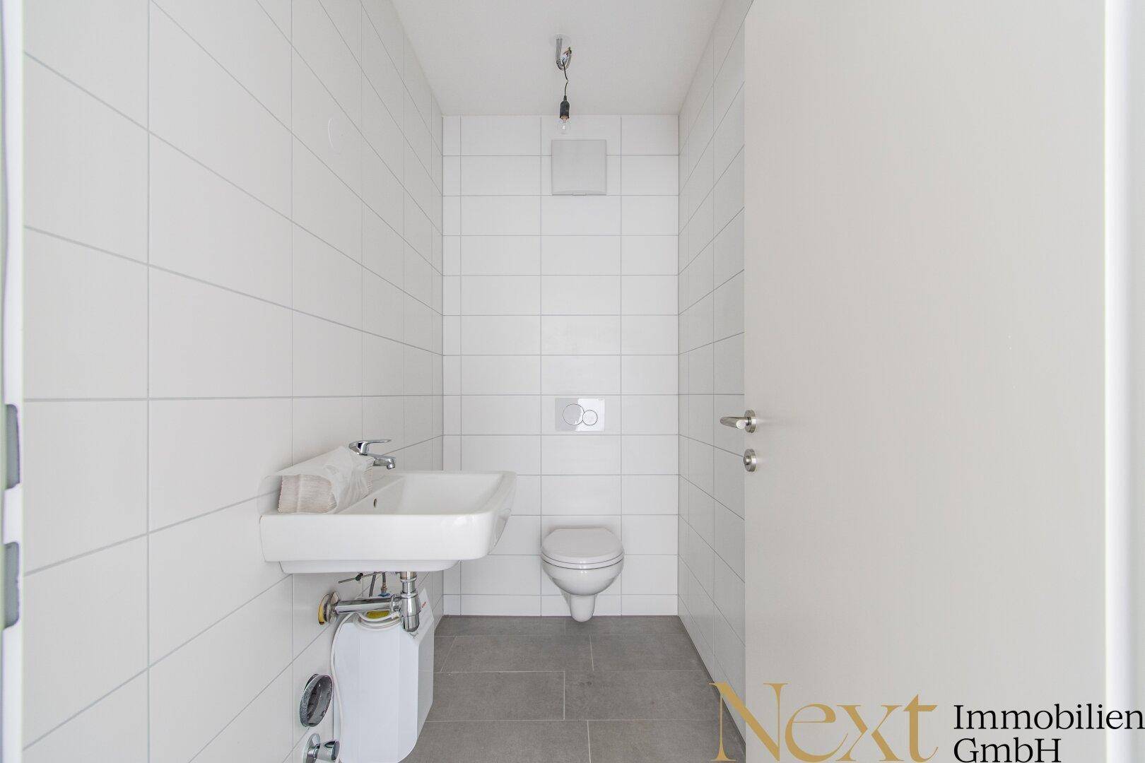 Modernes Gäste-WC mit weißen Wandfliesen, Hänge-WC und kleinem Waschbecken, in neuwertigem Zustand.