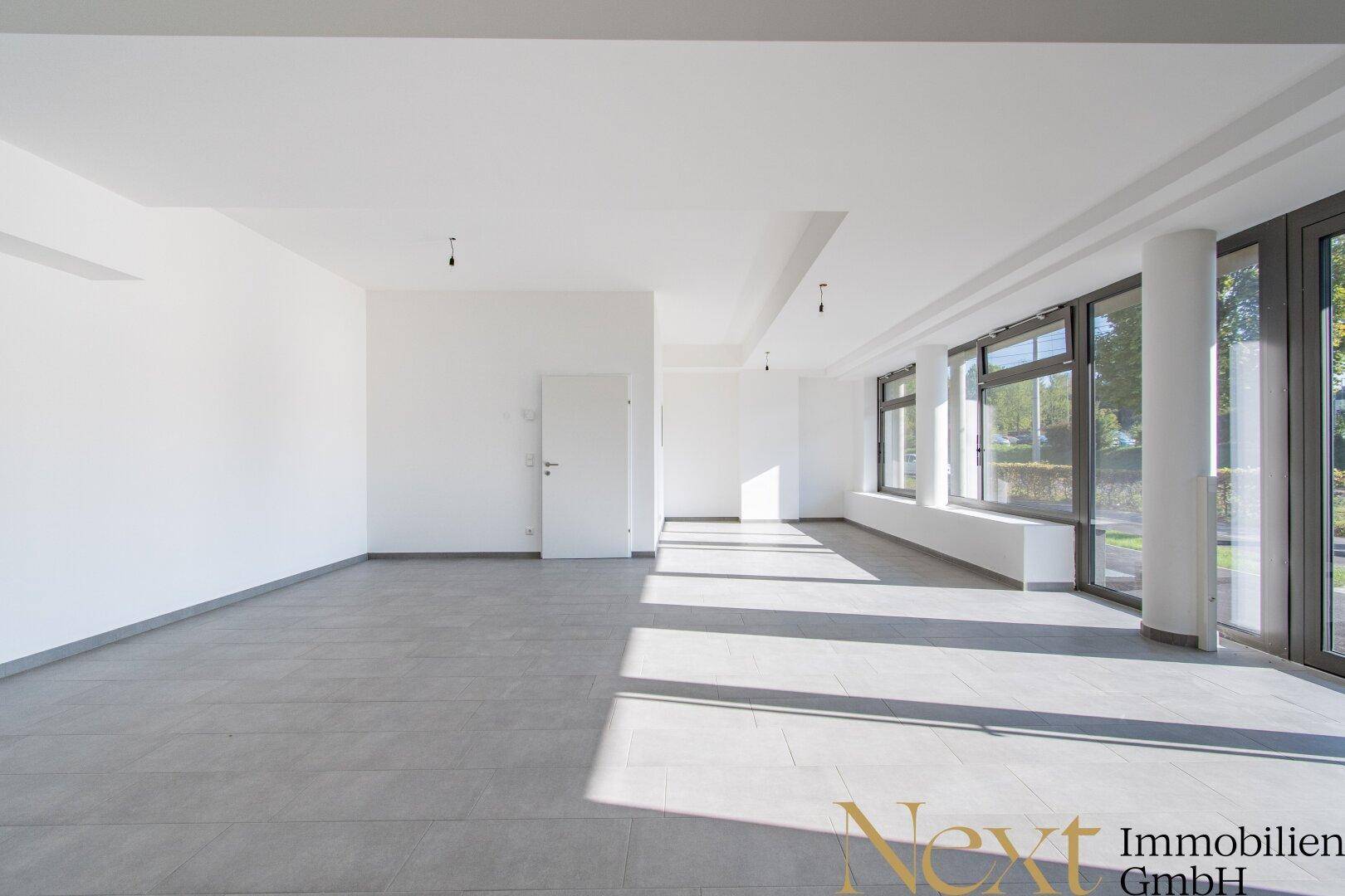 Heller, leerer Raum mit großen Fenstern und grauem Fliesenboden, ideal für Büro oder Gewerbe.