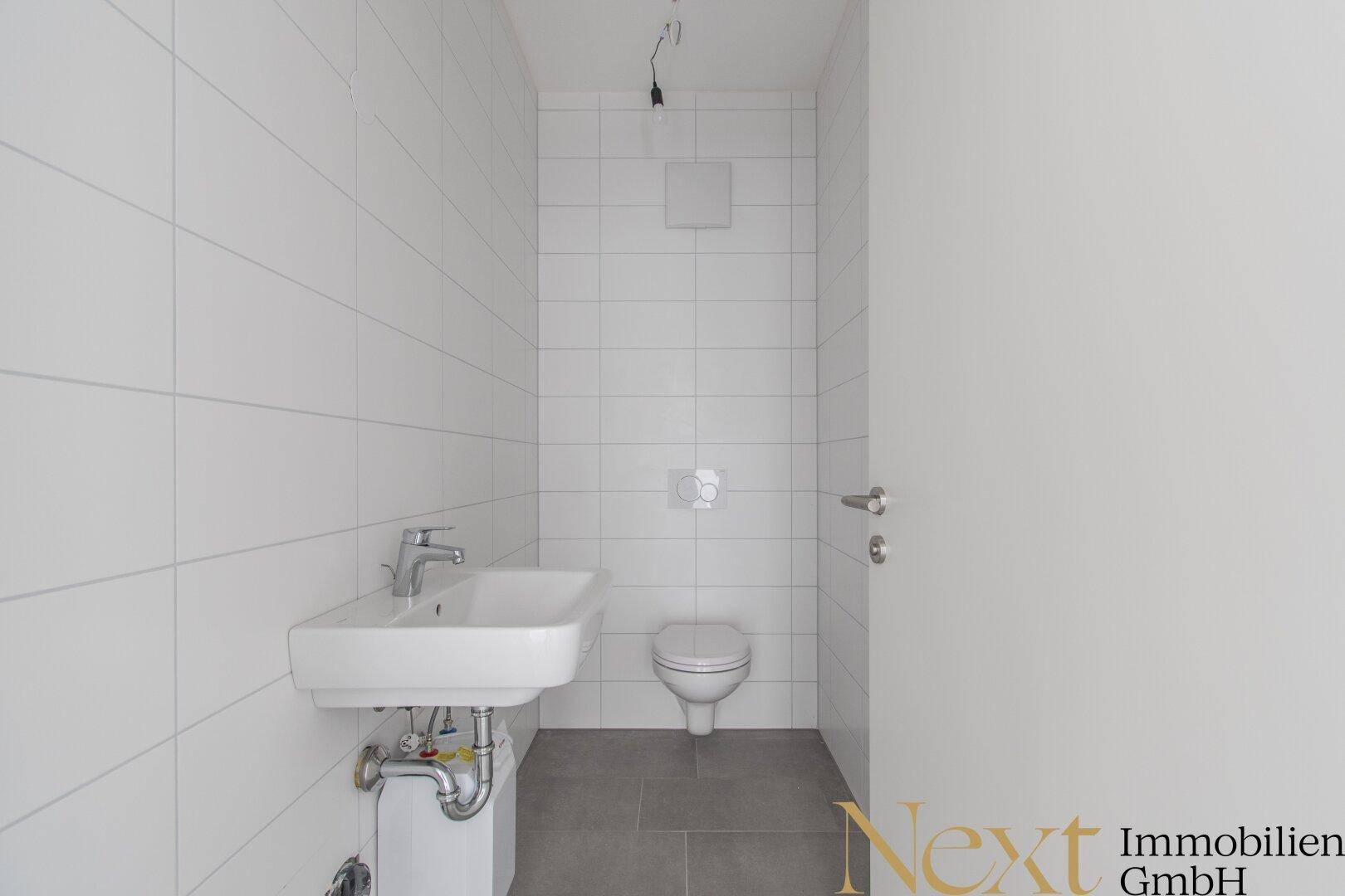 Modernes Gäste-WC mit weiß gefliesten Wänden, Hänge-WC und kleinem Waschbecken, in neuwertigem Zustand.