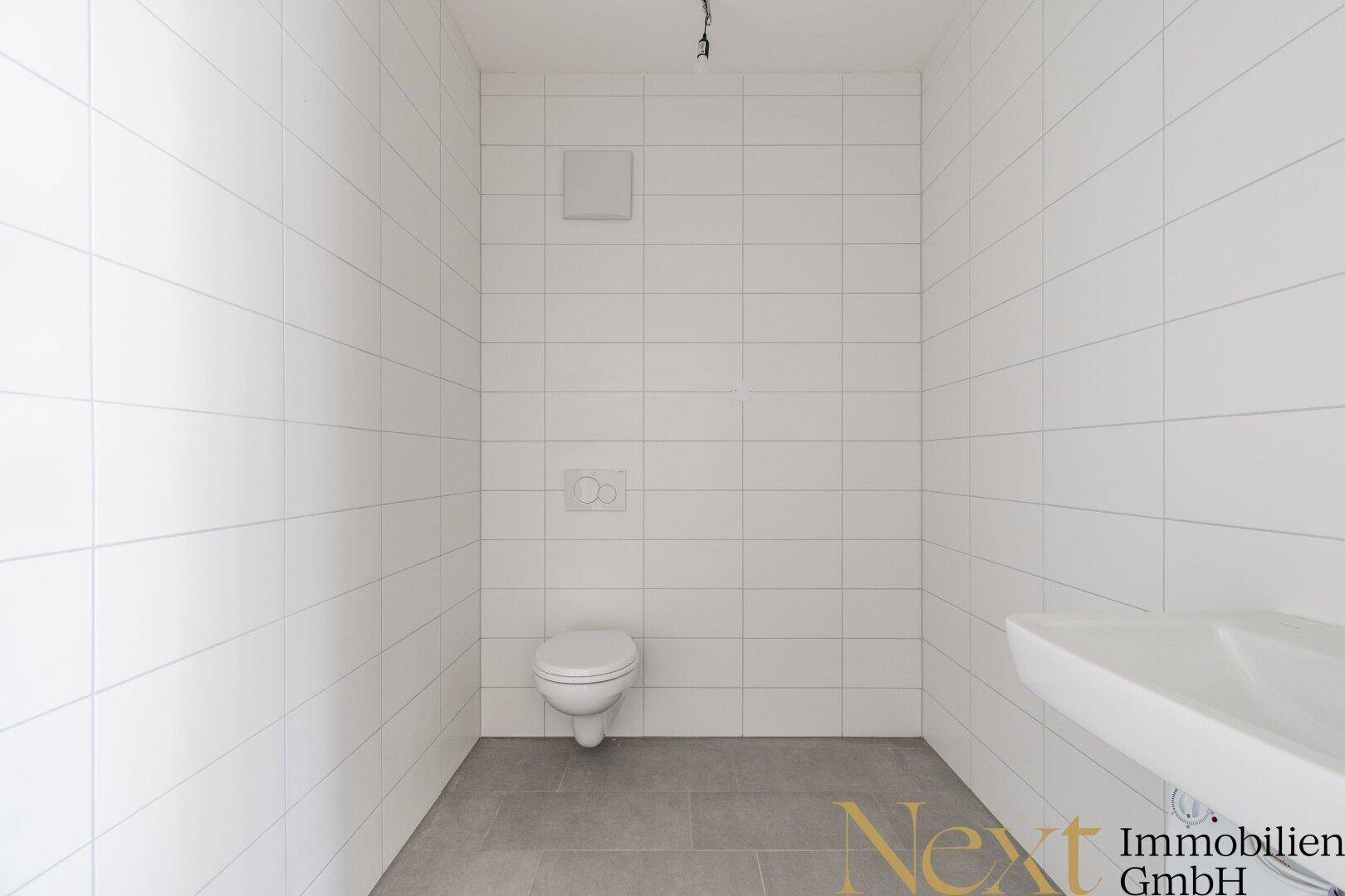 Sauberes und funktionales WC mit weißen Wandfliesen und grauem Boden, unbenutzt und gepflegt.