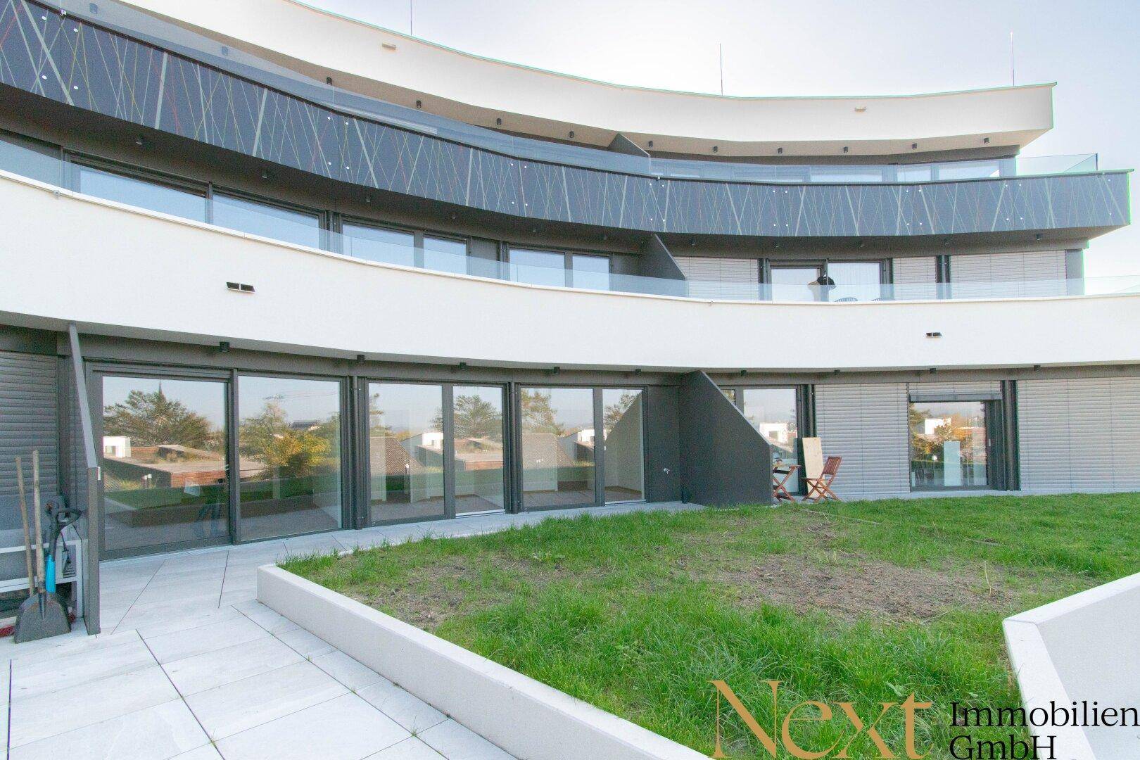 Moderne Architektur mit geschwungener Fassade, großen Fensterfronten und einer kleinen Grünfläche.