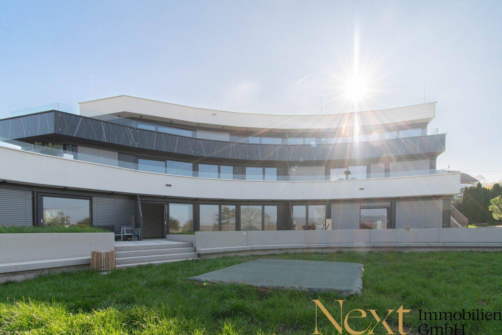 Sonnenbeschienene moderne Wohnanlage mit geschwungener Architektur und einer gepflegten Grünfläche.