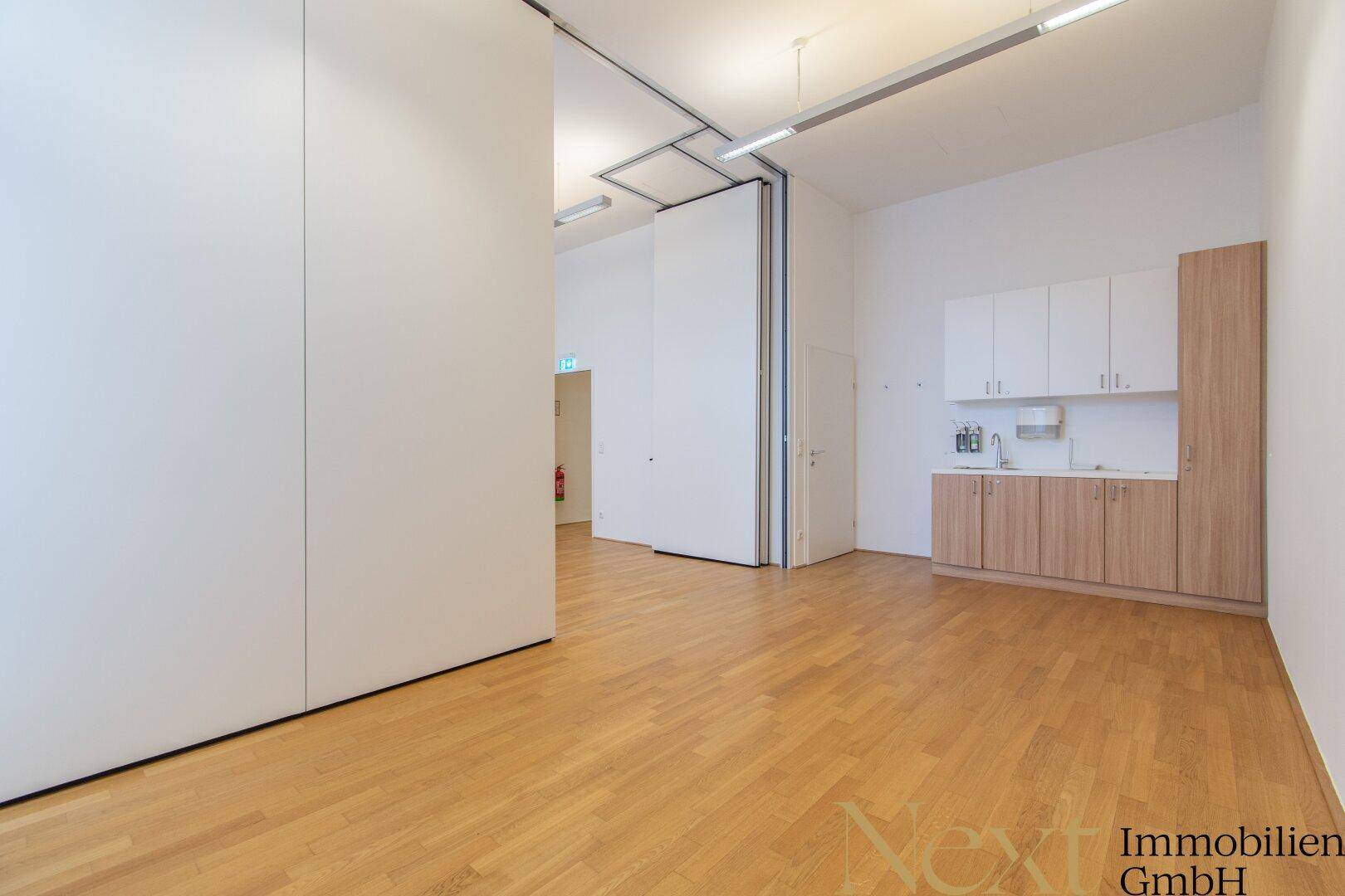 Großer, heller Bürobereich mit Holzboden, flexiblen Trennwänden und einer kleinen Teeküche.