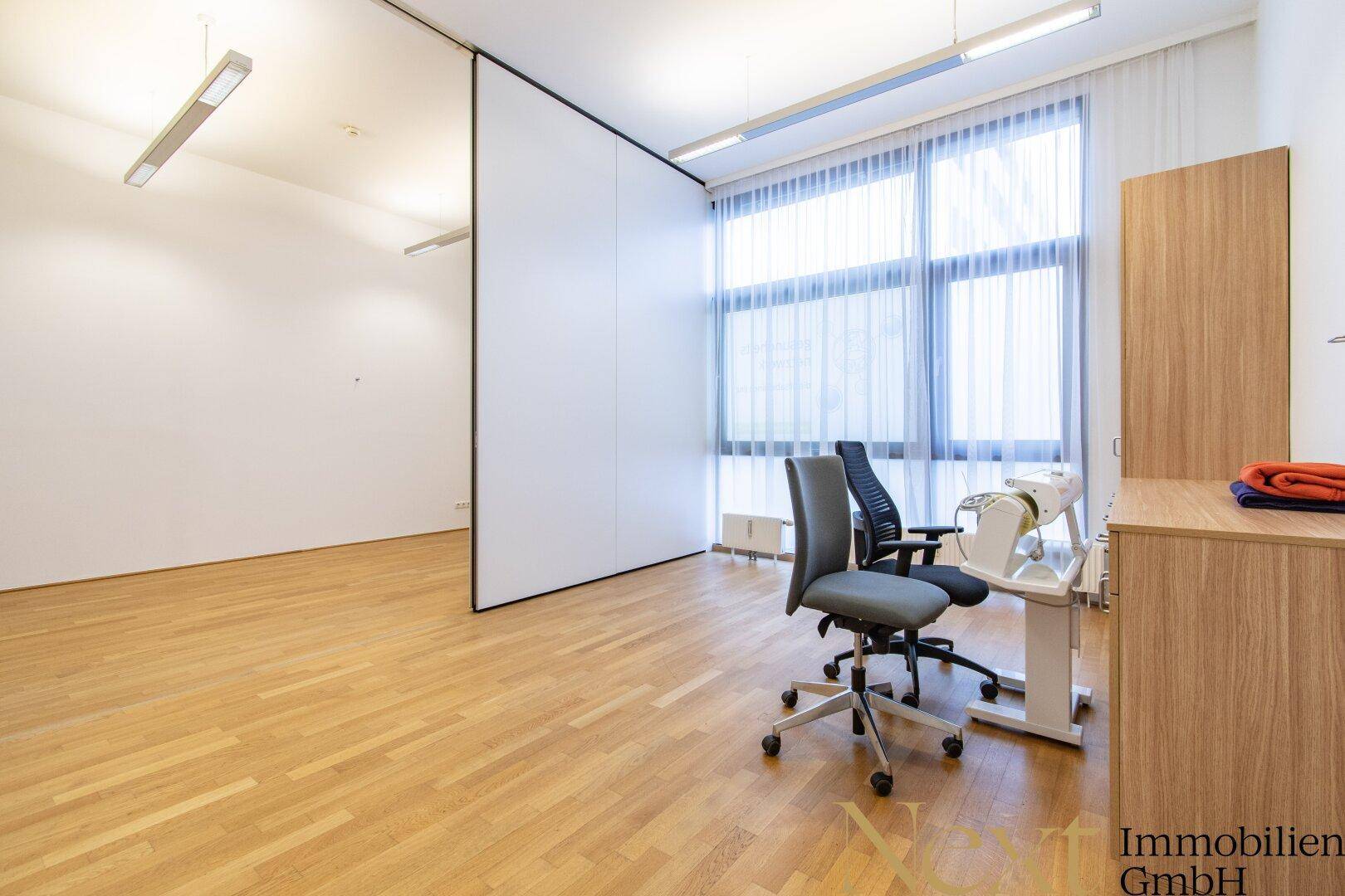Heller Büroraum mit Holzboden, großen Fenstern und flexibler Raumtrennung.