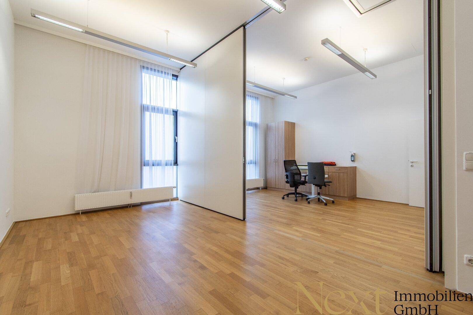 Geräumiger Bürobereich mit Holzboden, großen Fenstern und flexiblen Trennwänden für verschiedene Arbeitsbereiche.