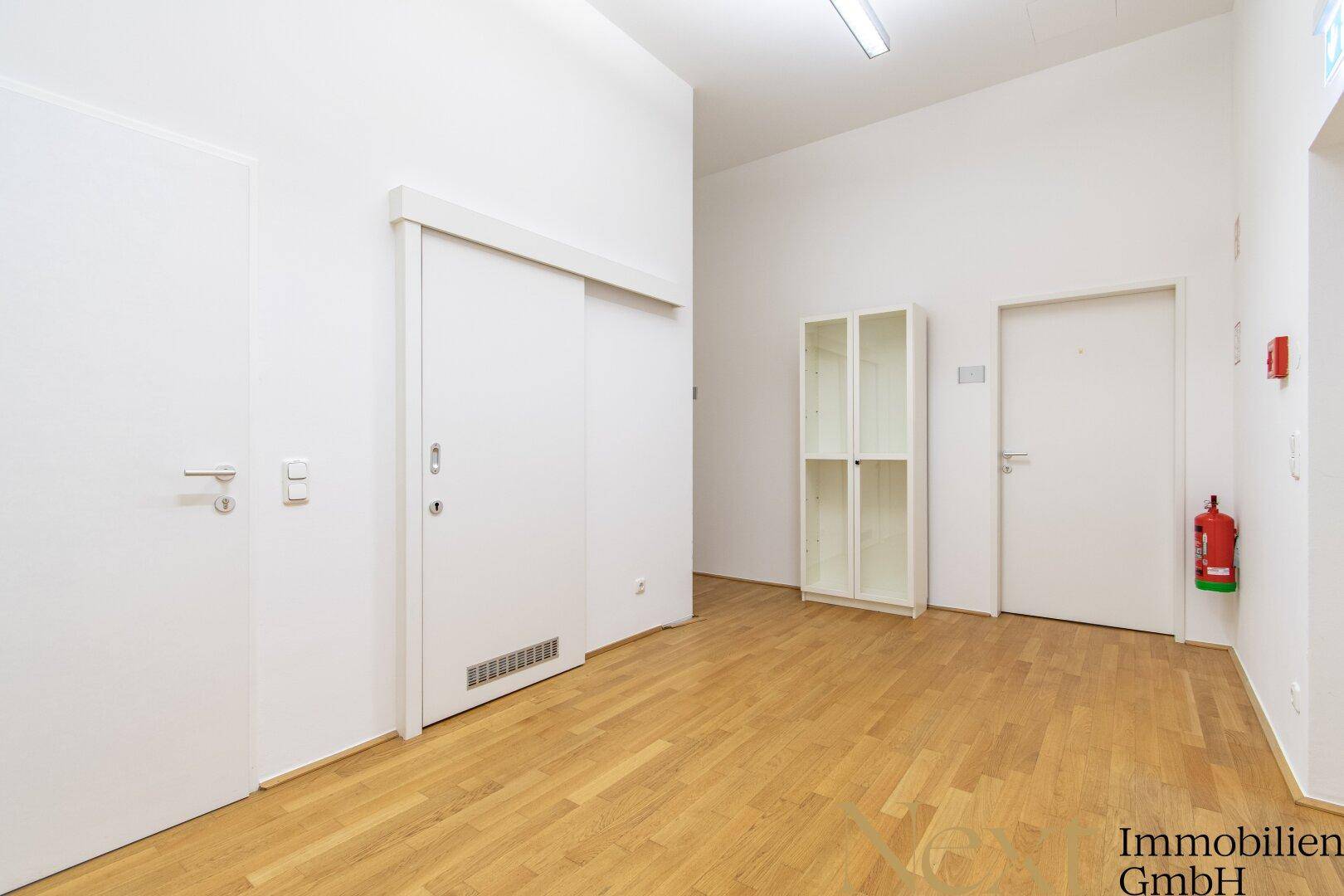 Heller Flurbereich in einem Bürogebäude mit Holzboden und weißen Türen.