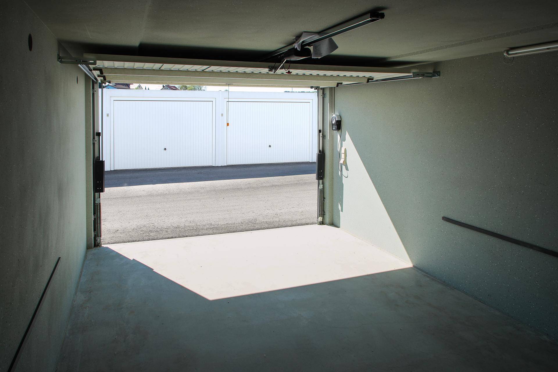 Innenansicht einer Garage mit geöffnetem Tor, das den Blick auf weitere Garagen und den Außenbereich freigibt.