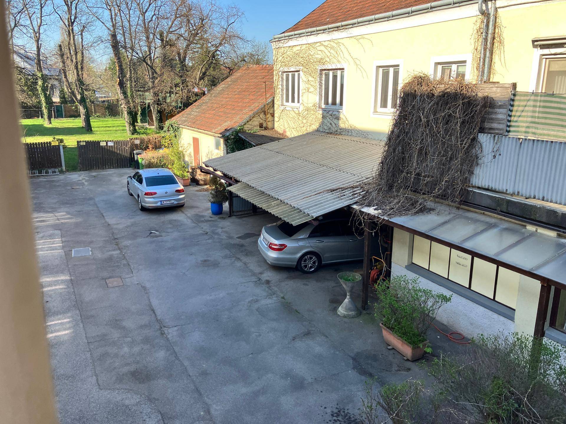 Erhöhte Ansicht eines Hofbereichs mit geparkten Autos, überdachten Stellplätzen und Gebäuden im Hintergrund.